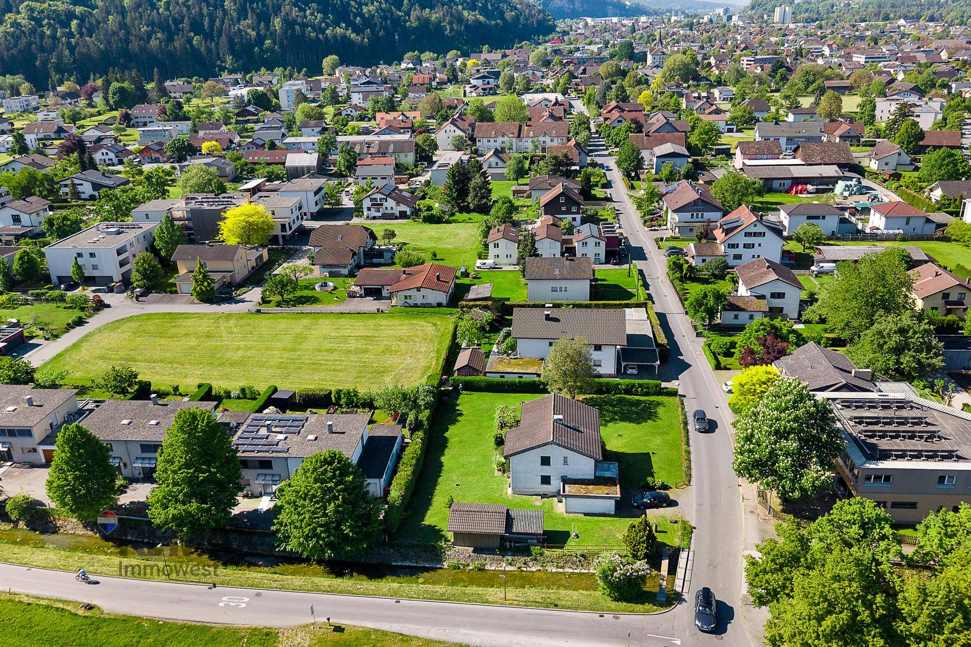 Panoramablick aus der Luft auf eine Wohnsiedlung mit weiten Grünflächen und Bergen im Hintergrund.