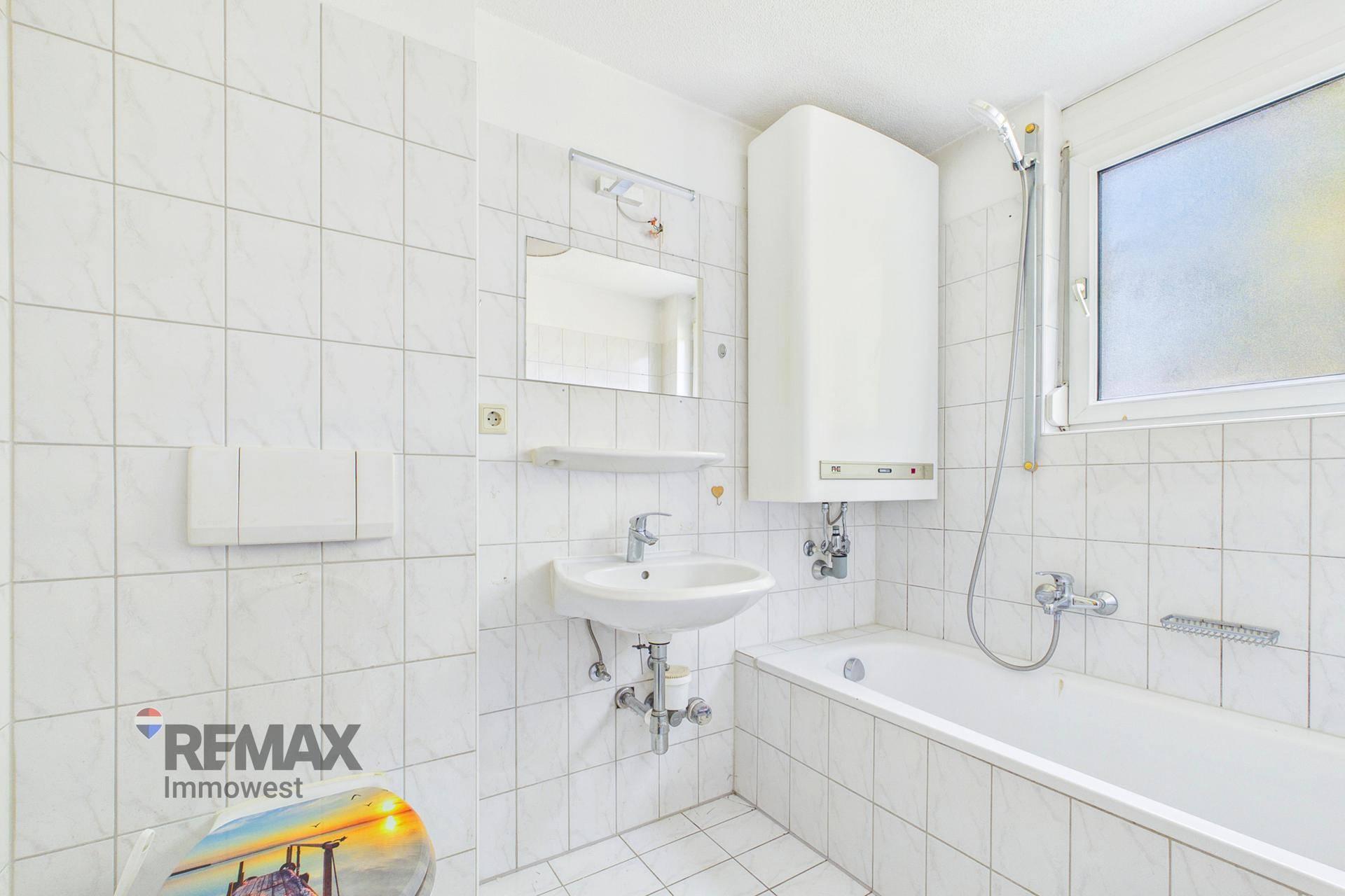 Gefliestes Badezimmer mit Badewanne, Waschbecken und Fenster für natürliche Belüftung.