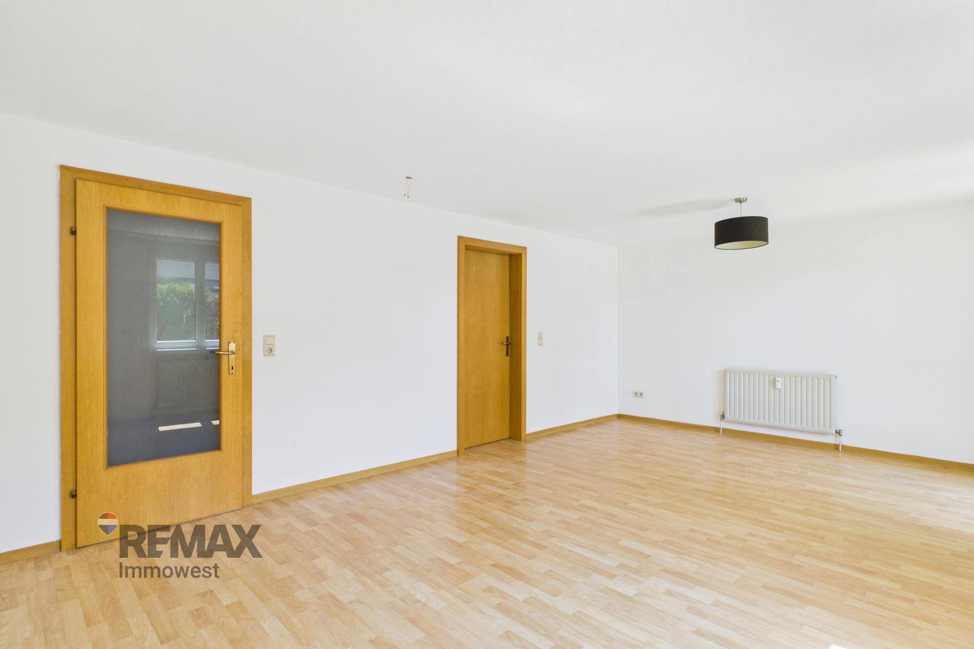 Leeres Wohnzimmer mit hellem Parkettboden und zwei Holztüren, bereit zur individuellen Gestaltung.