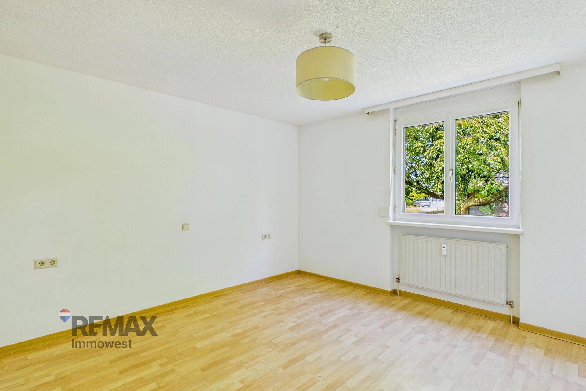 Helles Schlafzimmer mit Parkettboden und großem Fenster, das viel Tageslicht hereinlässt.