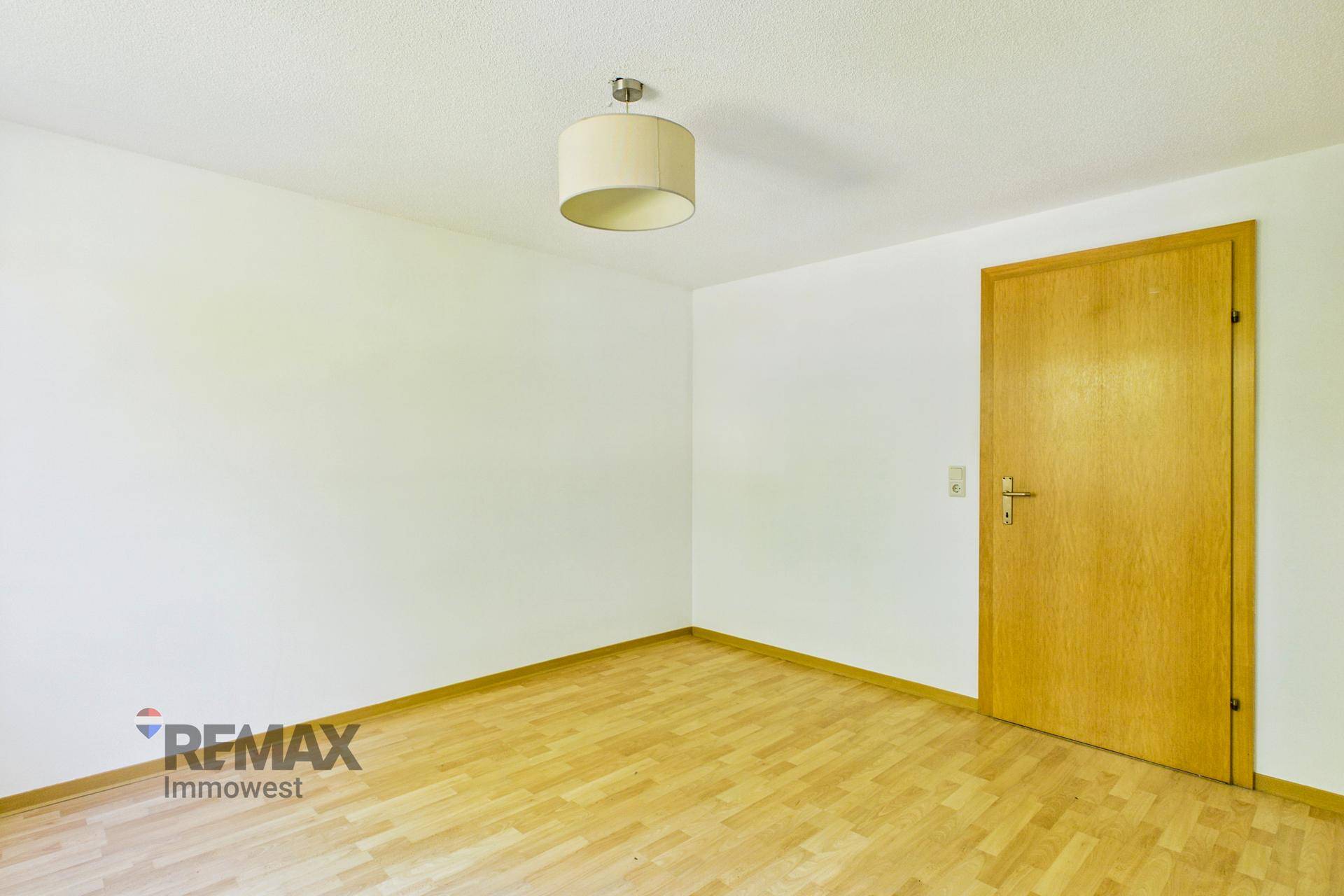 Leeres Schlafzimmer mit hellem Parkettboden und einer Holztür, bereit zur Einrichtung.
