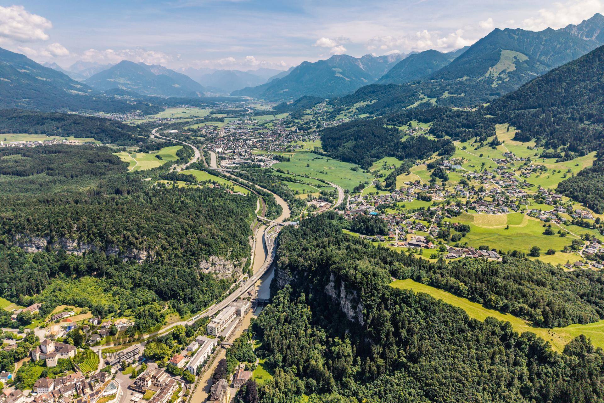 Beeindruckende Luftaufnahme eines Flusstals mit Autobahn, Ortschaften und majestätischen Bergen.