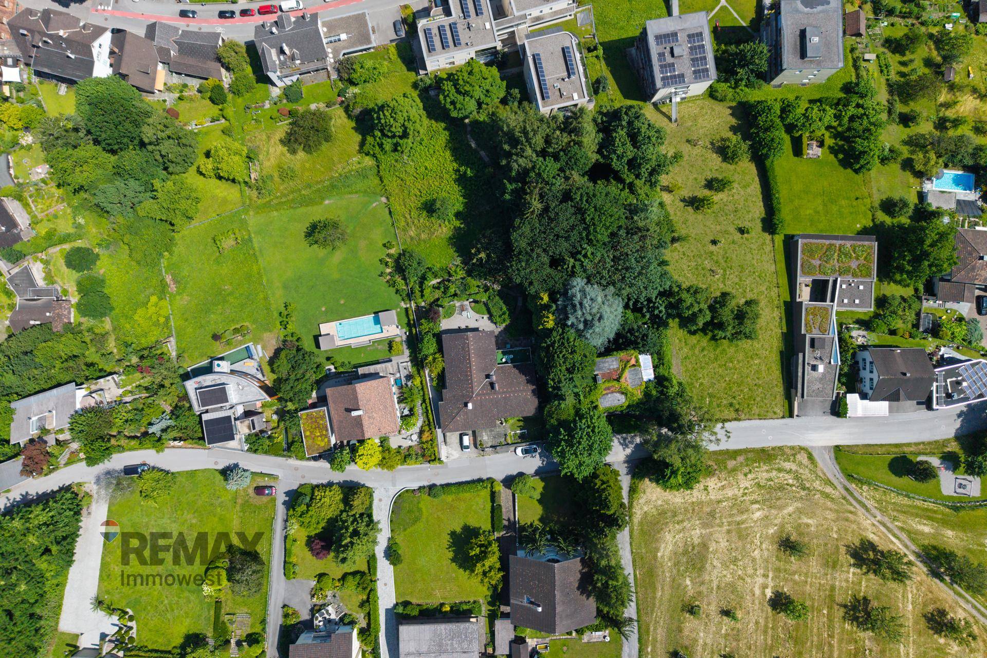 Weitläufige Luftaufnahme eines Wohngebiets mit Häusern, Gärten und Straßen in sonniger Umgebung.