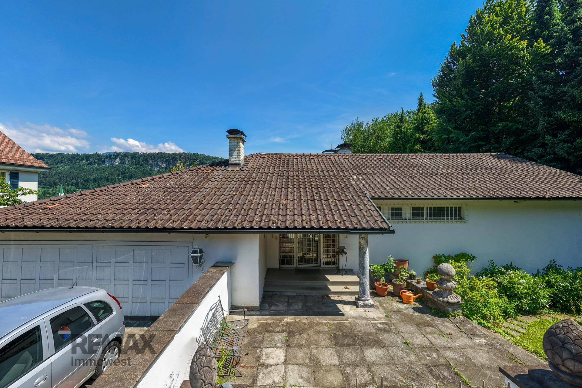 Eingangsbereich des Hauses mit Garage und gepflasterter Auffahrt unter blauem Himmel.