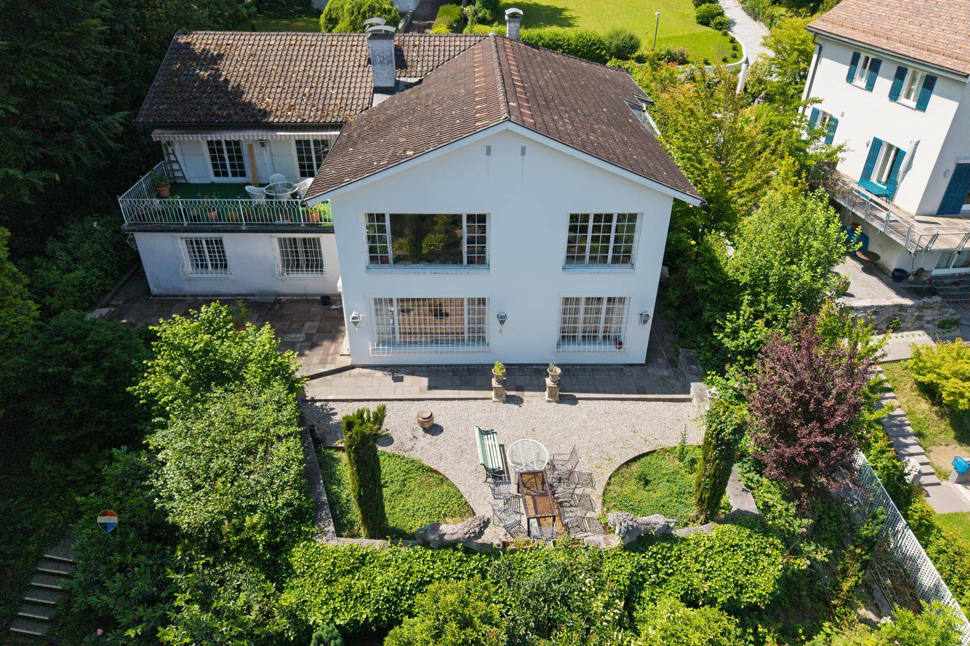 Luftaufnahme des Hauses mit weißer Fassade, Gartenbereich und einem Nachbarhaus mit Balkon.