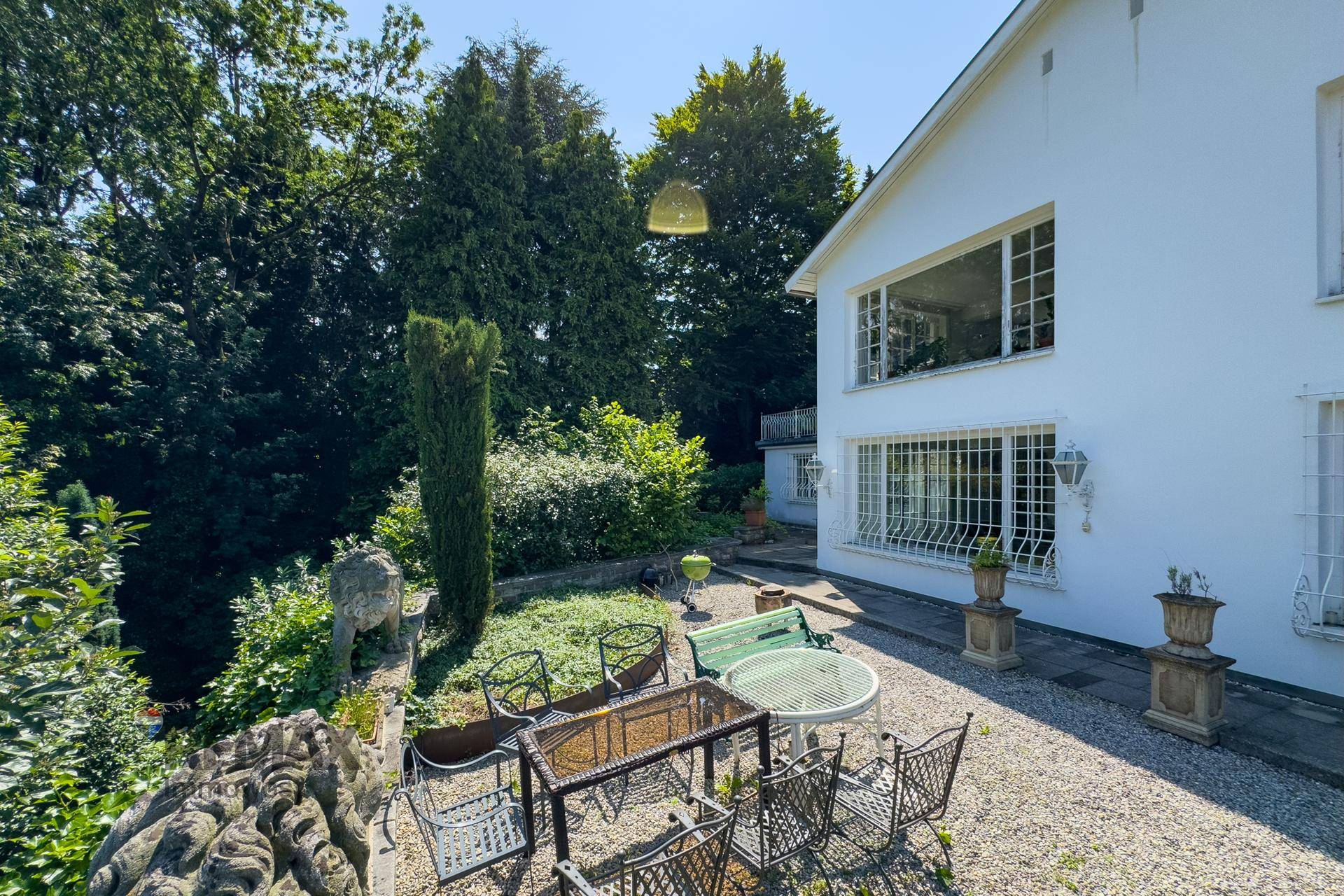 Gartenbereich mit Sitzgelegenheiten und Blick auf die Hausfassade und die umliegenden Bäume.