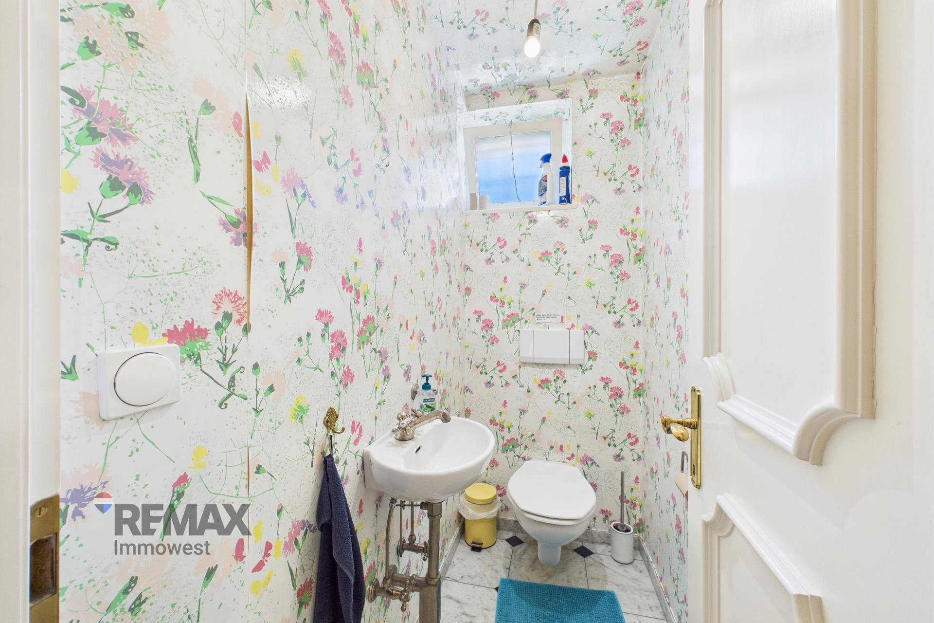 Gäste-WC mit floraler Tapete, kleinem Waschbecken und Toilette.