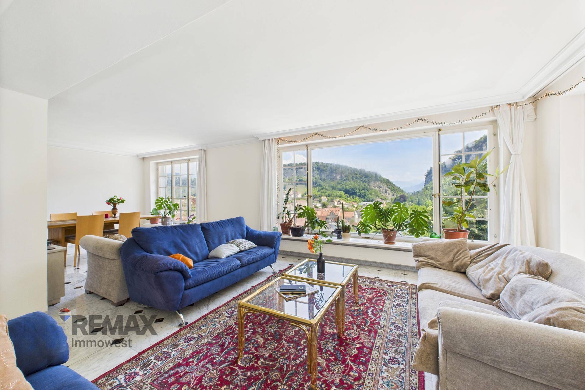 Wohnzimmer mit blauen Sofas, Couchtisch und großen Fenstern mit Blick ins Grüne.