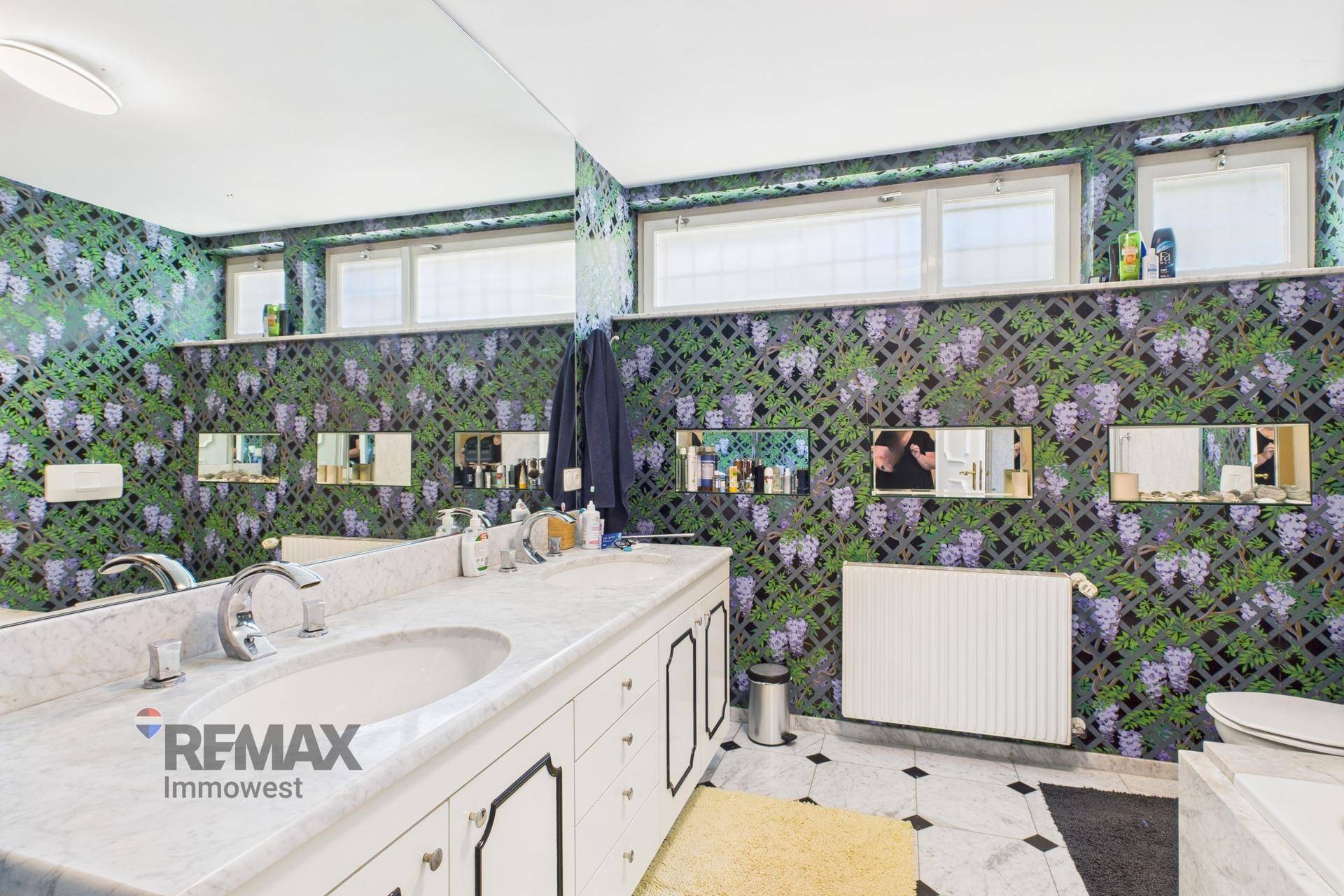 Badezimmer mit floraler Tapete, Doppelwaschbecken und Marmor-Arbeitsplatte.