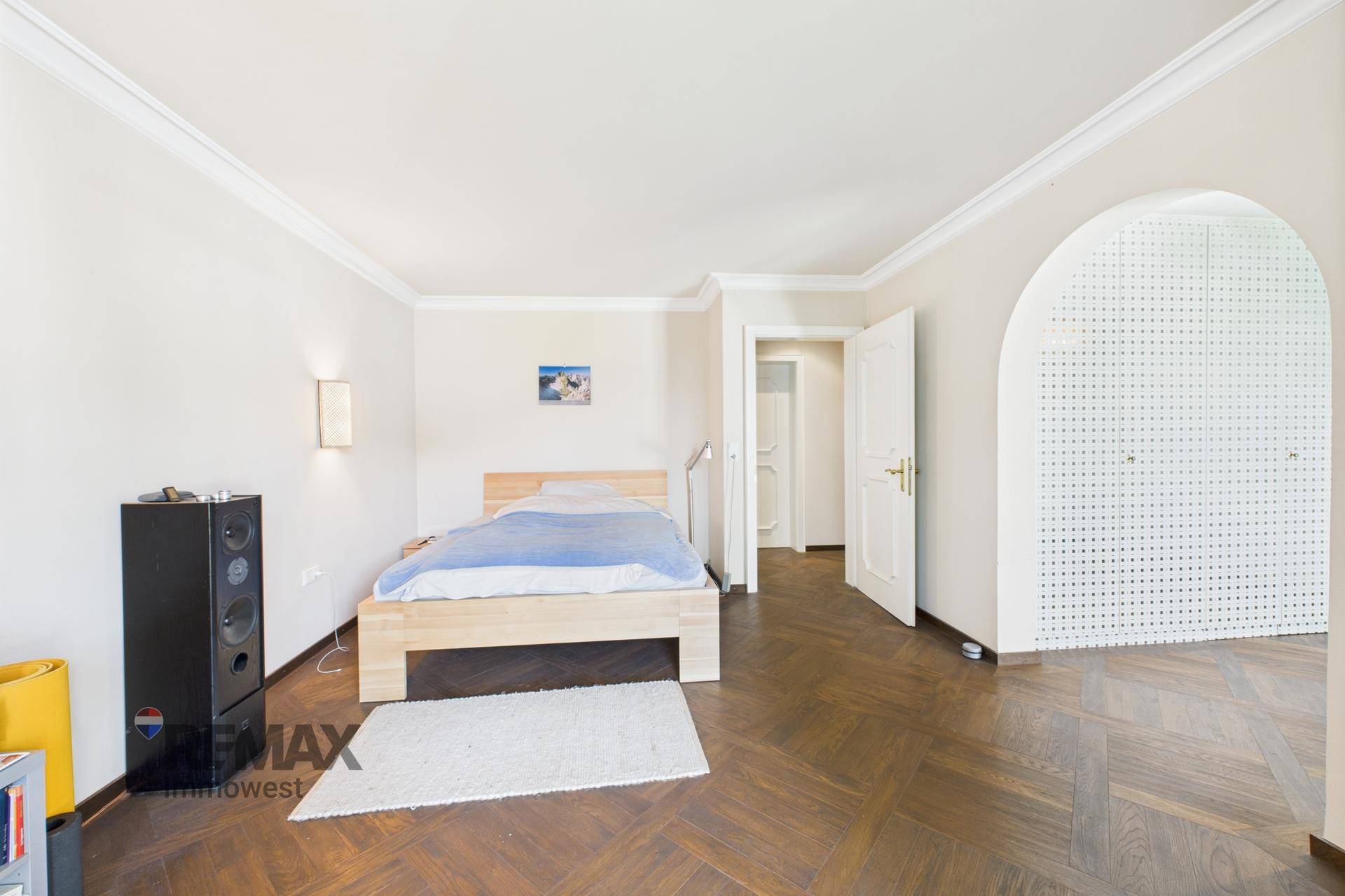 Schlafzimmer mit Parkettboden, weiß gestrichenen Wänden und einem Bogen zum Nebenraum.