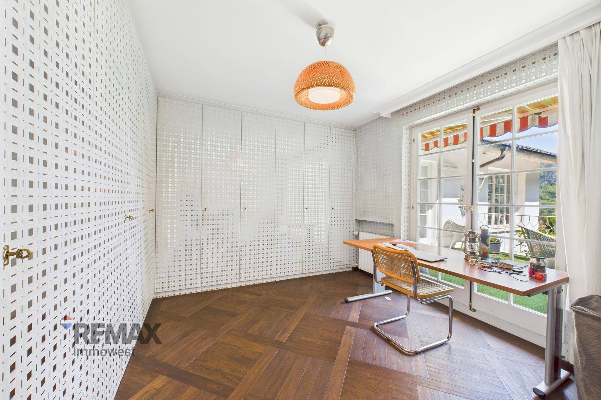 Arbeitszimmer mit Parkettboden, Einbauschränken und Zugang zu einem sonnigen Außenbereich.