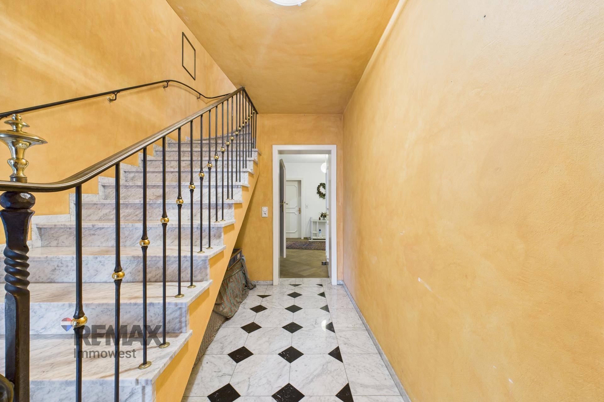 Geräumiger Flur mit Marmortreppe, schmiedeeisernem Geländer und gelben Wänden.