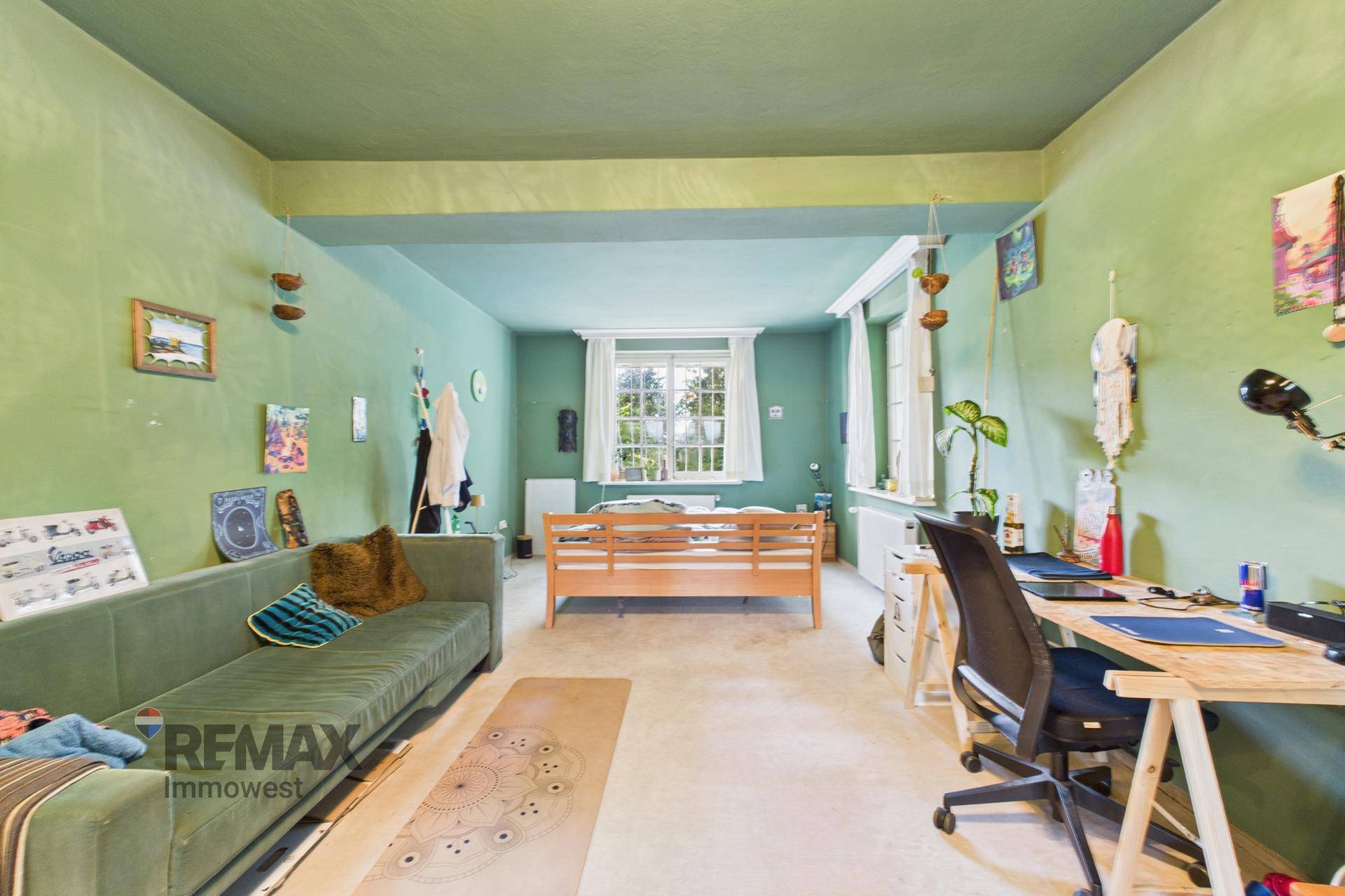 Geräumiges Schlafzimmer mit grünen Wänden, Sofa und Arbeitsbereich, bietet viel Platz.