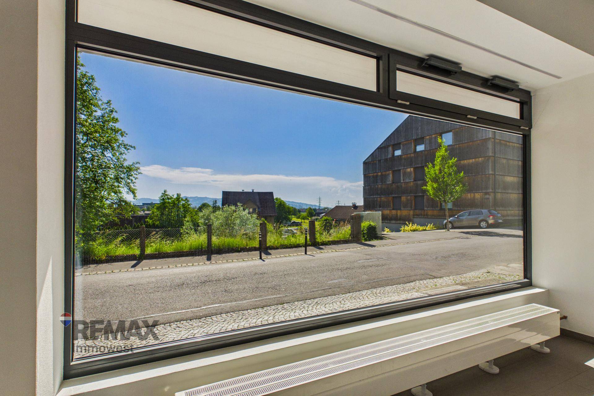 Weitläufiger Ausblick aus dem Fenster auf die Straße, ein modernes Gebäude und die hügelige Landschaft.