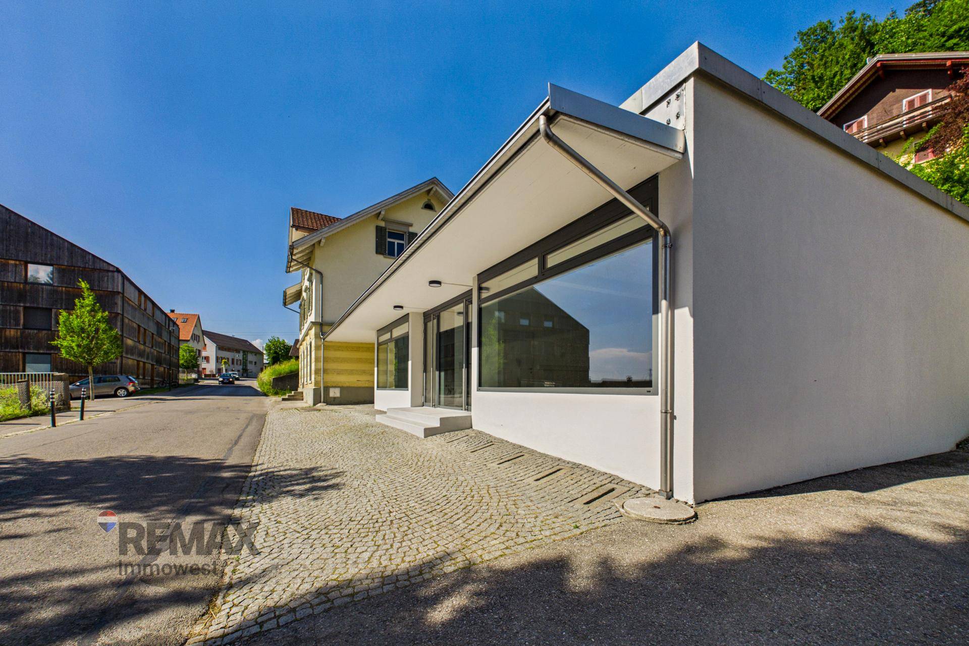 Seitenansicht des modernen Geschäftsgebäudes mit großen Fenstern und einem gepflasterten Vorplatz.