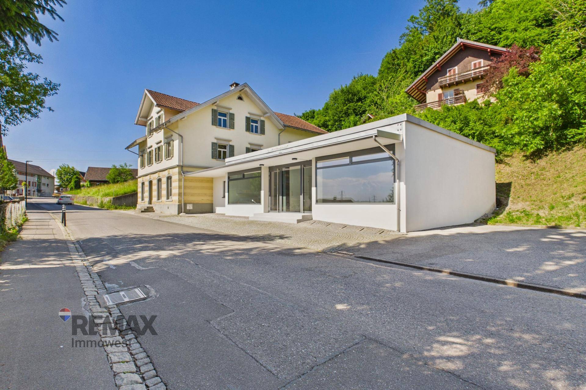 Außenansicht des Gebäudes mit Geschäftsflächen und angrenzendem Altbau an einer Straße.