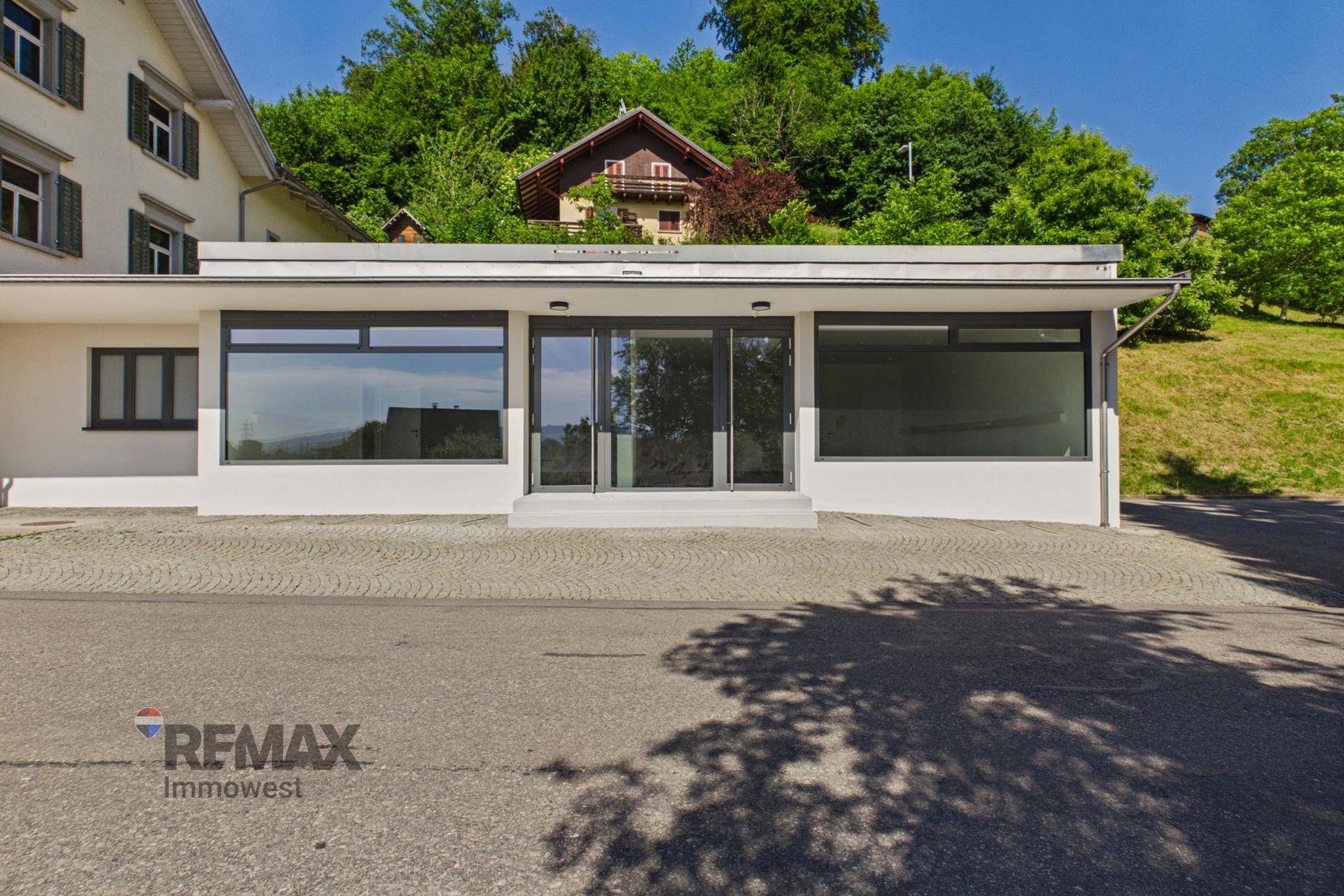 Frontansicht des Geschäftsgebäudes mit großen Schaufenstern und Eingang, umgeben von Grün.