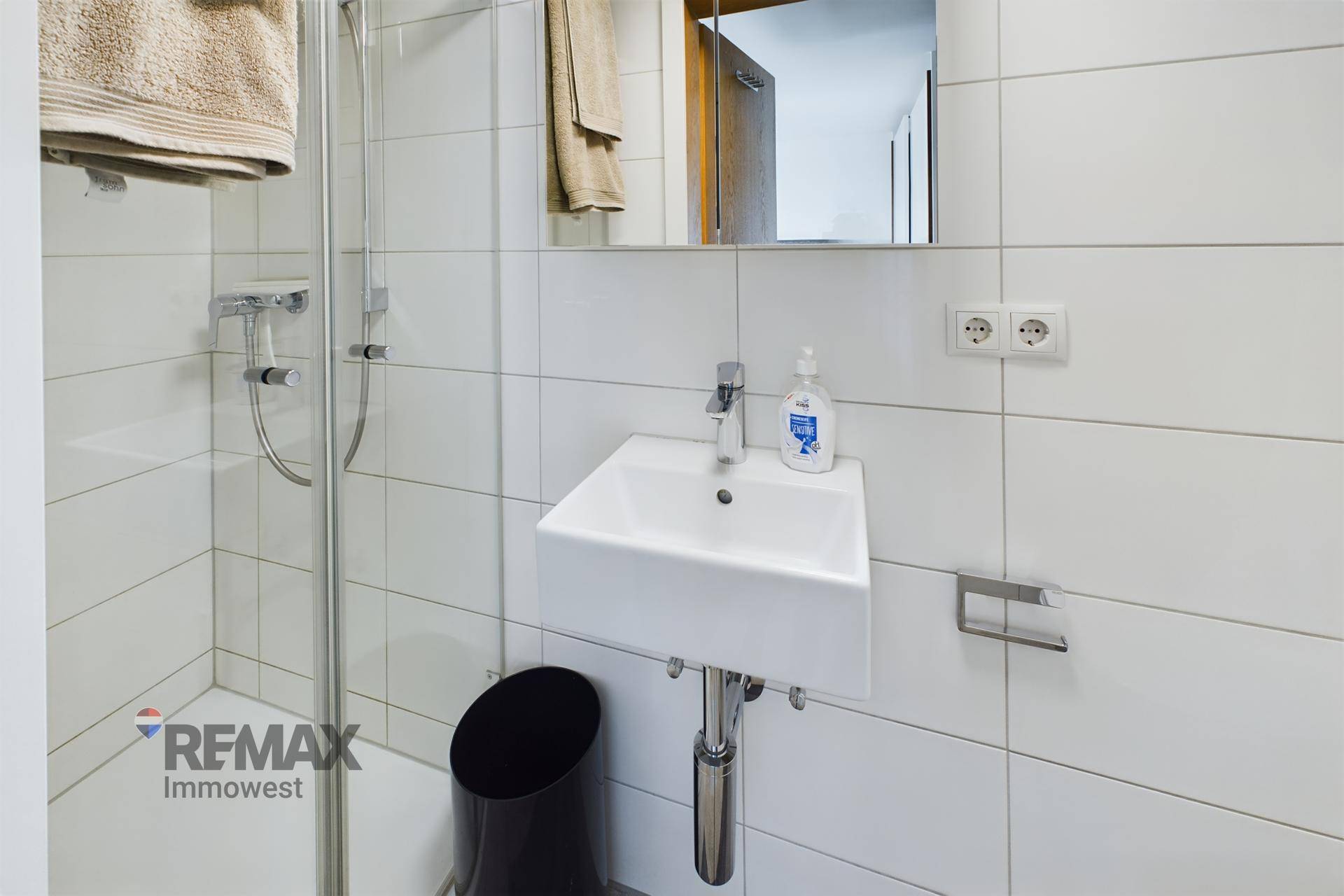Modernes Badezimmer mit Dusche, Waschbecken, Spiegelschrank und weißen Fliesen.