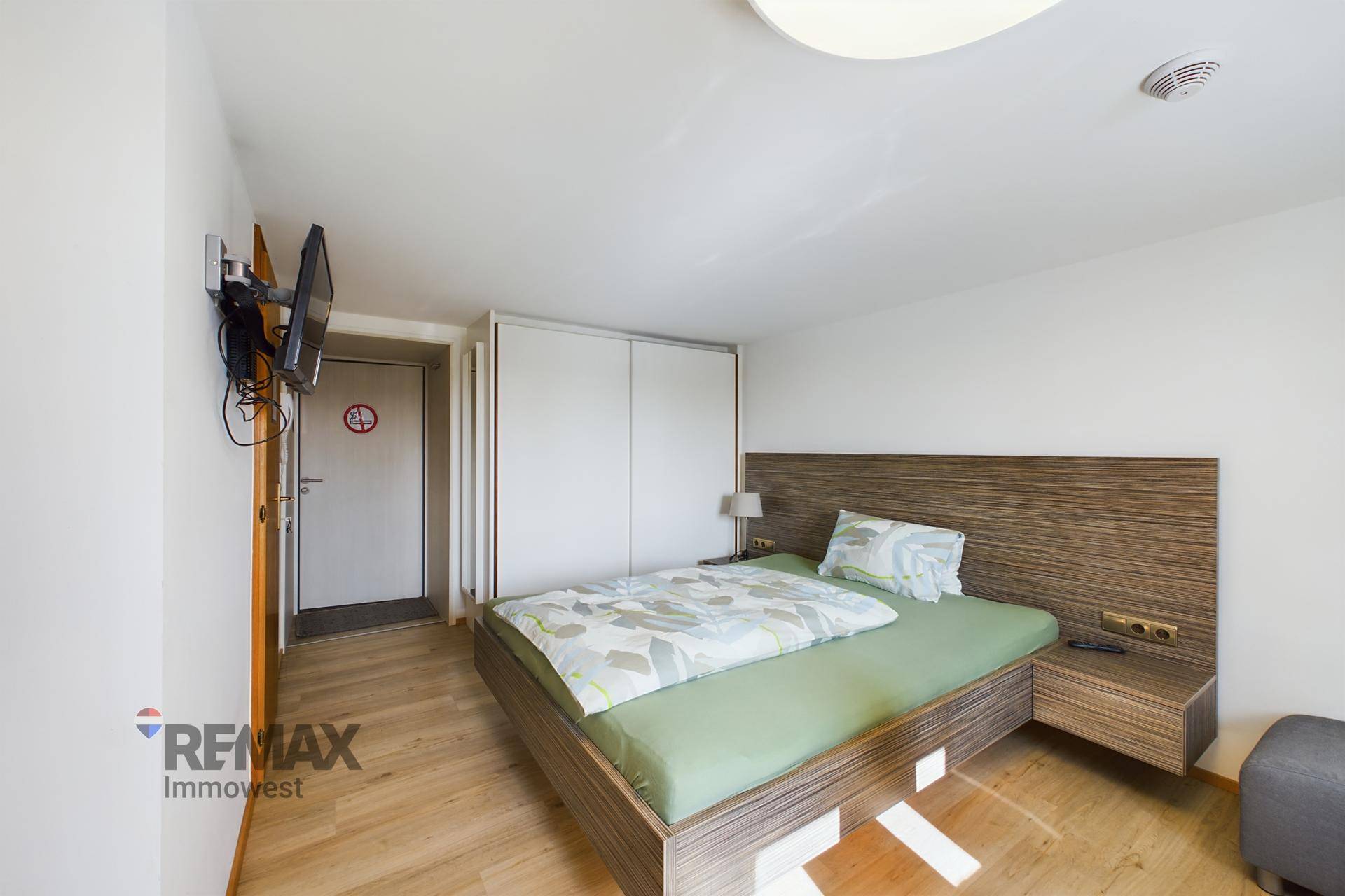Schlafzimmer mit Holzbett, integrierten weißen Schränken und Wandfernseher.