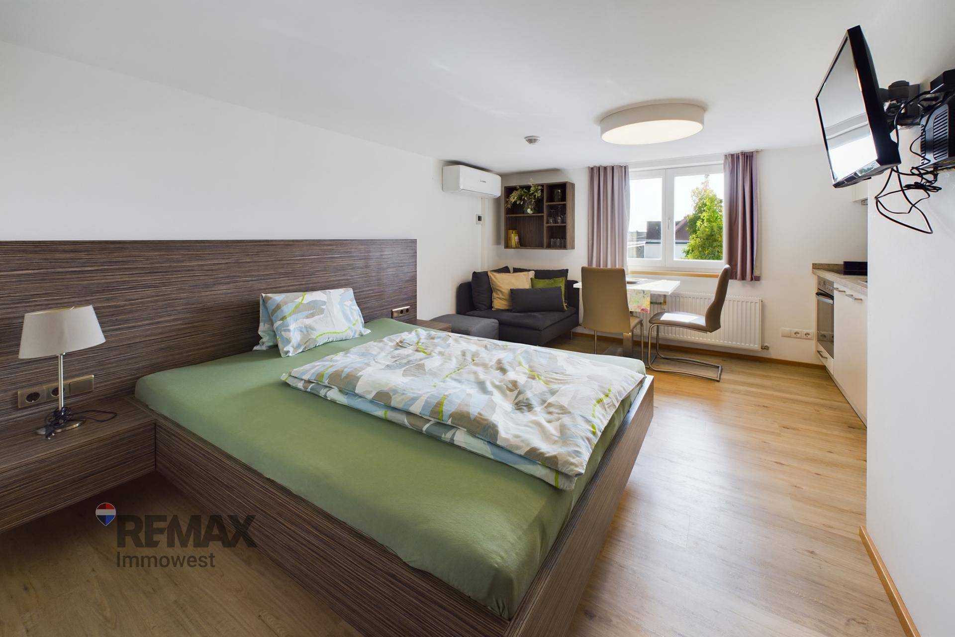 Geräumiges Schlafzimmer mit Holzbett, Sofa, Esstisch und Blick nach draußen.