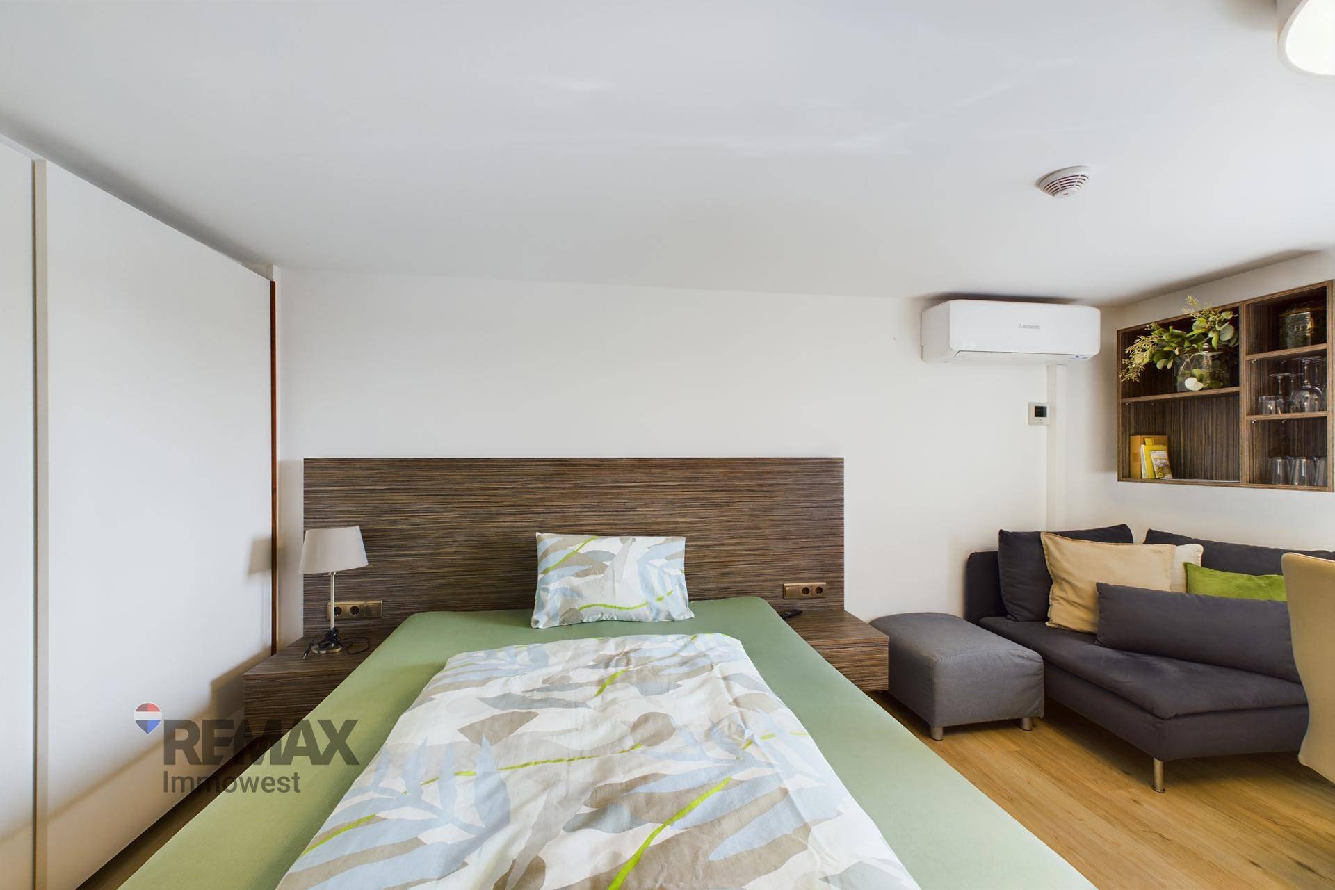 Gemütlicher Schlafbereich mit Holzbett, Sofa, Wandregal und Klimaanlage.