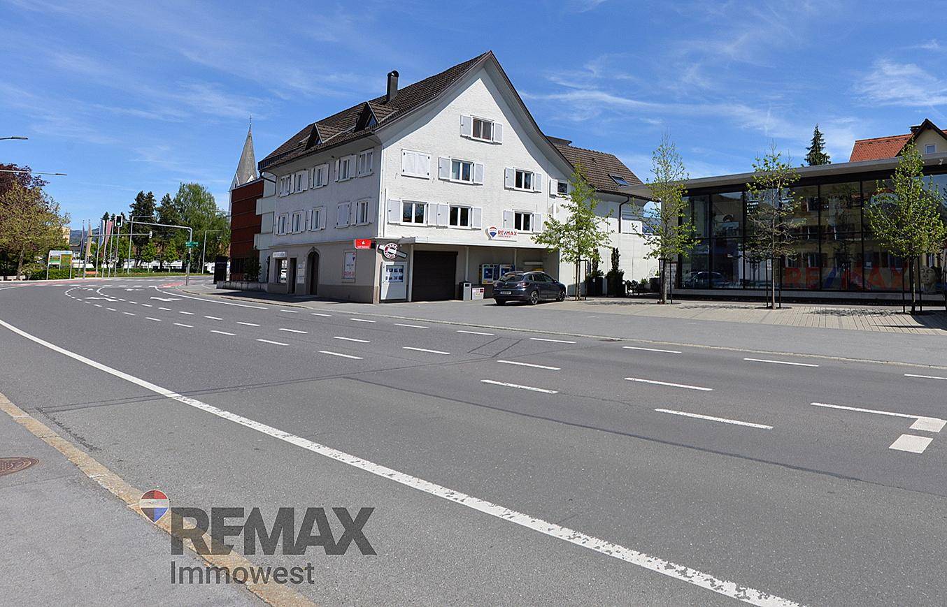 Traditionelles Gebäude mit weißer Fassade, blauen Fensterläden und Satteldach an einer Straße.
