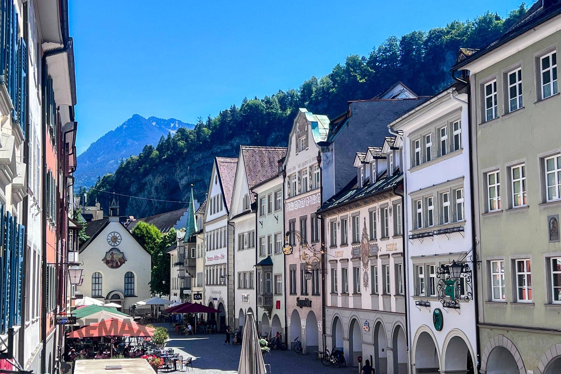 Malerische Altstadtgasse mit historischen Gebäuden und Bergblick im Hintergrund.