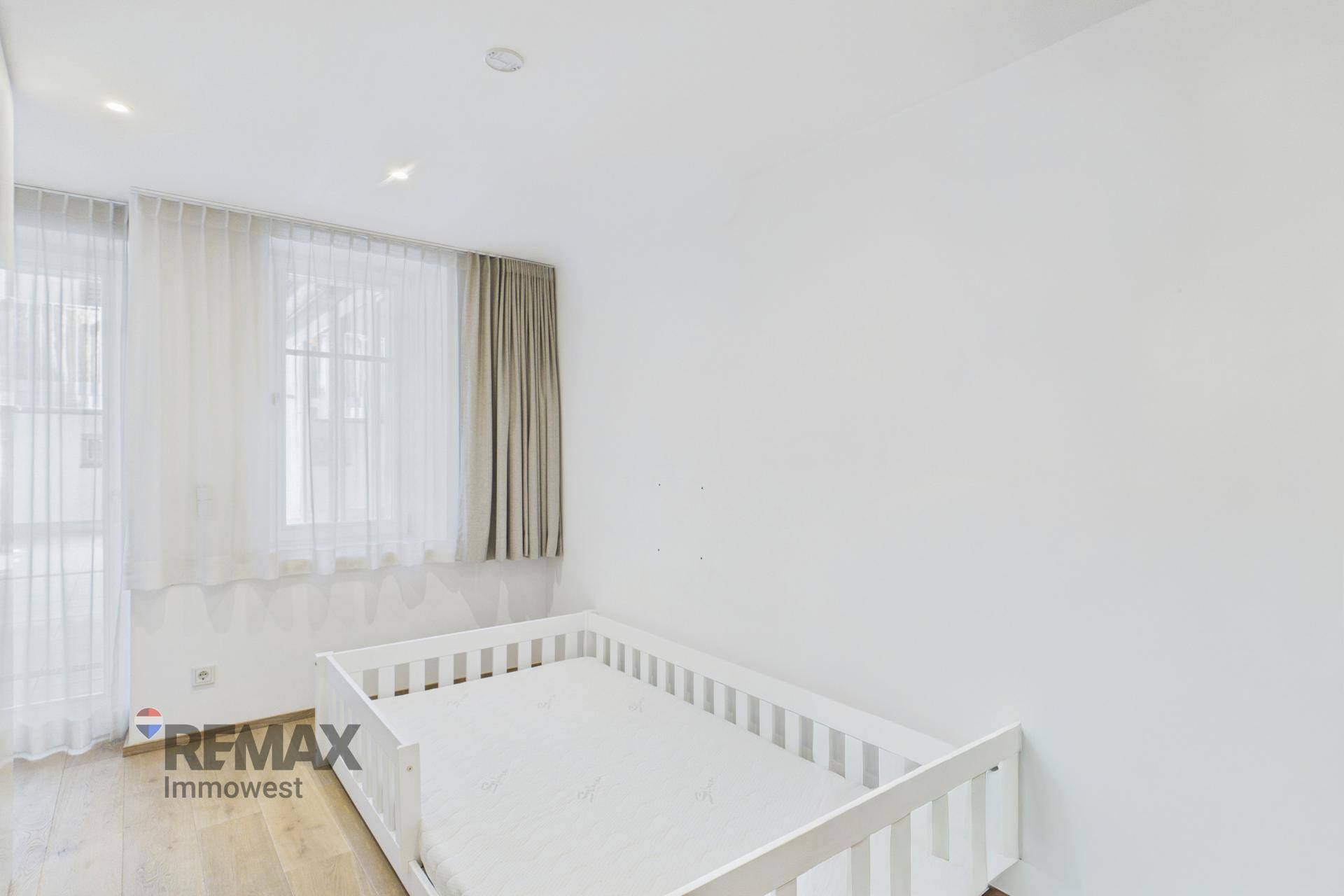 Helles Kinderzimmer mit weißem Gitterbett und großen Fenstern für viel Tageslicht.