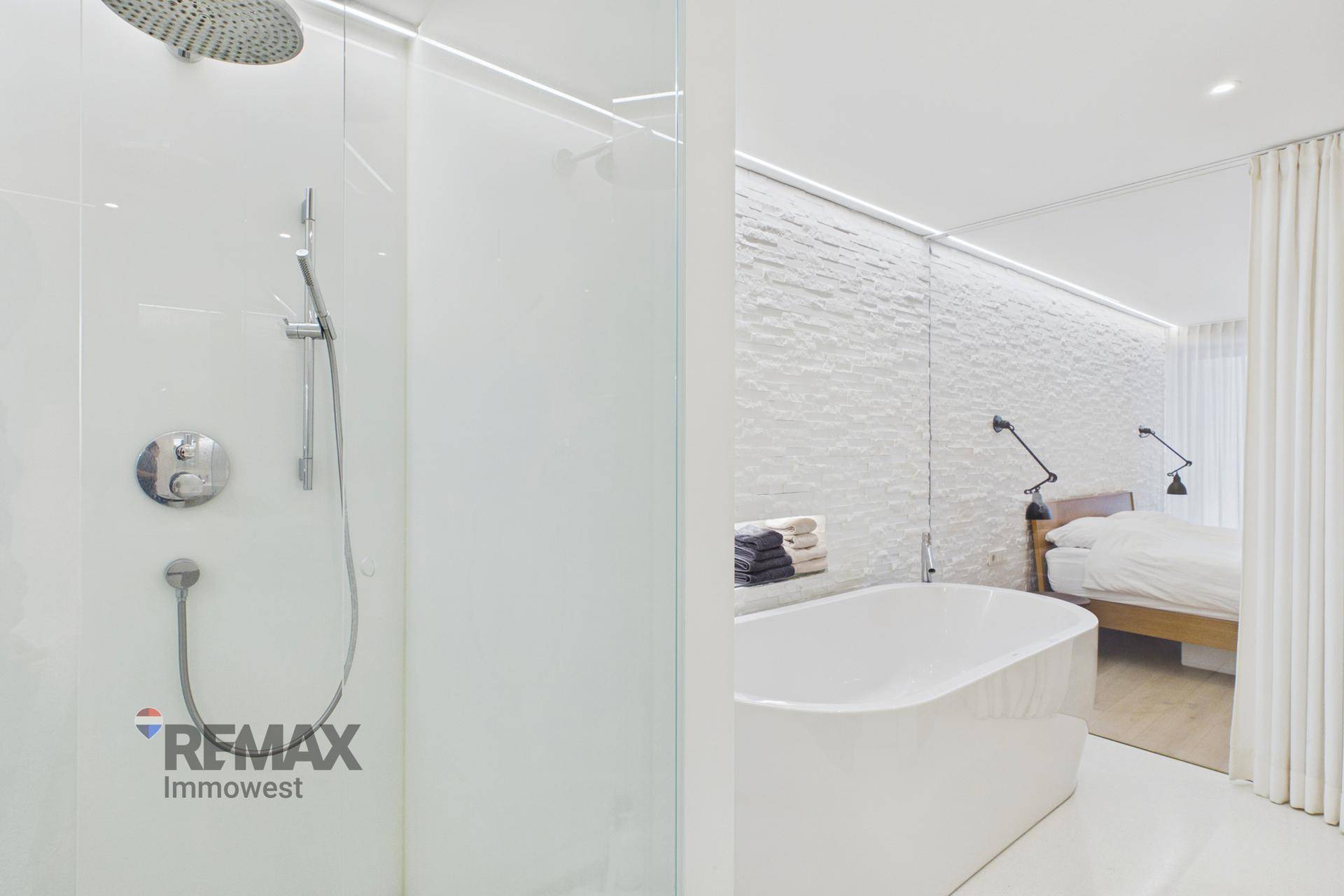 Elegantes Badezimmer mit Regendusche und freistehender Badewanne, offen zum Schlafzimmer.
