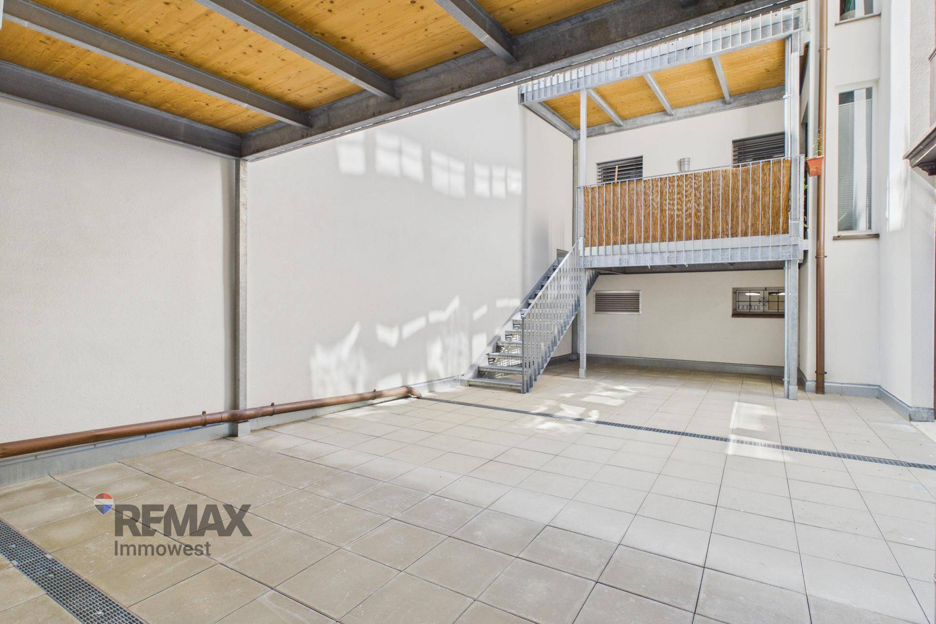 Große geflieste Terrasse mit Metalltreppe und überdachtem Bereich im Freien.
