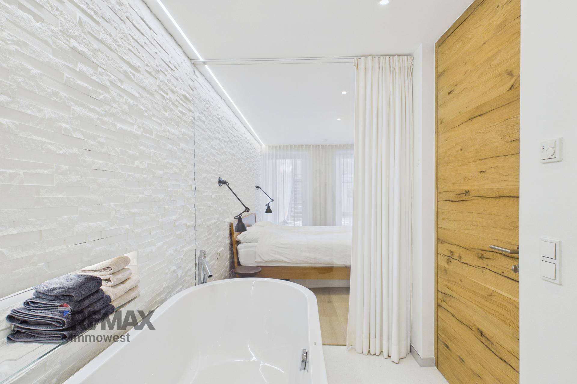 Offenes Badezimmer mit Badewanne und Blick ins Schlafzimmer, moderne Holztür.