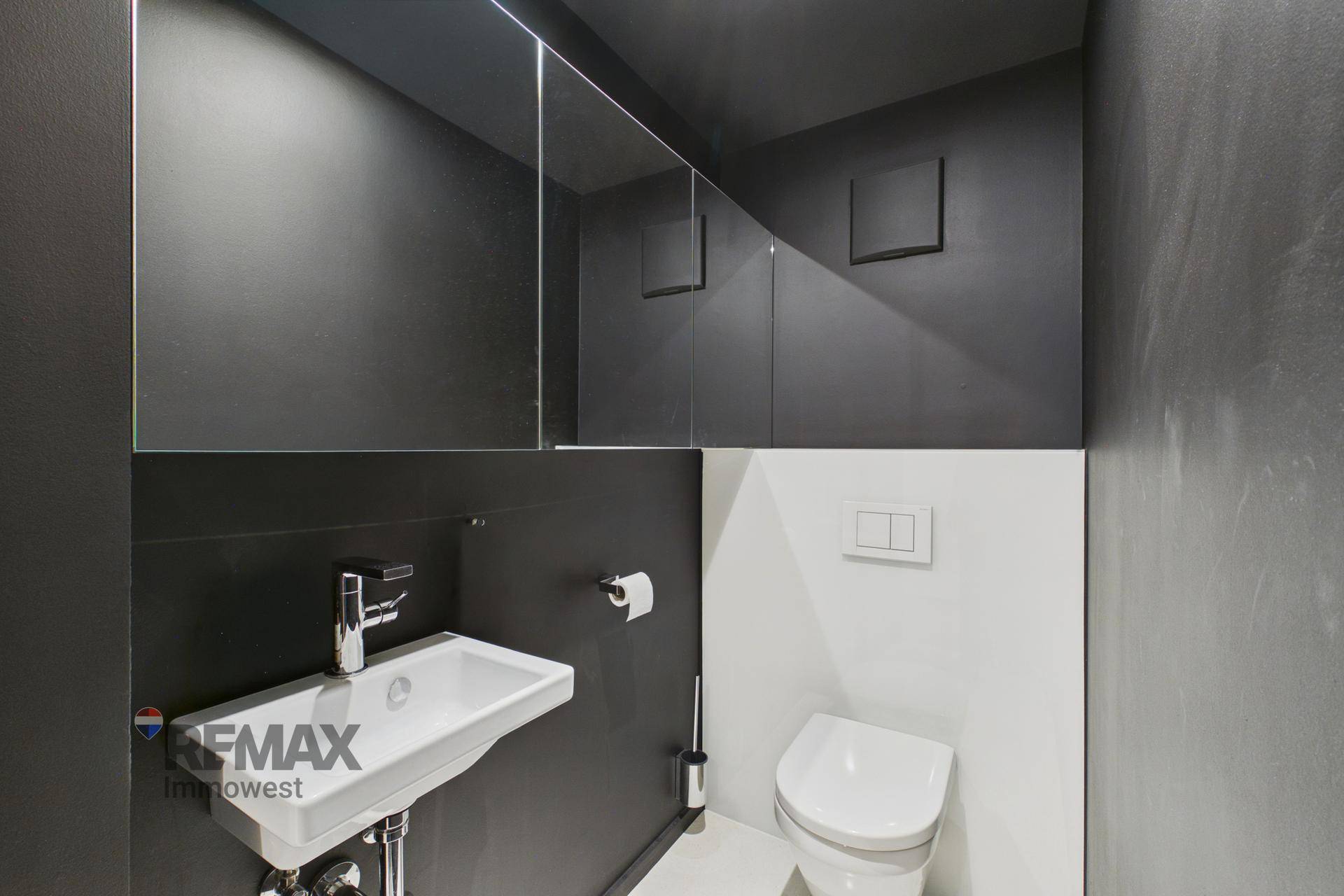 Modernes Gäste-WC mit dunklen Wänden, wandhängender Toilette und kleinem Waschbecken.