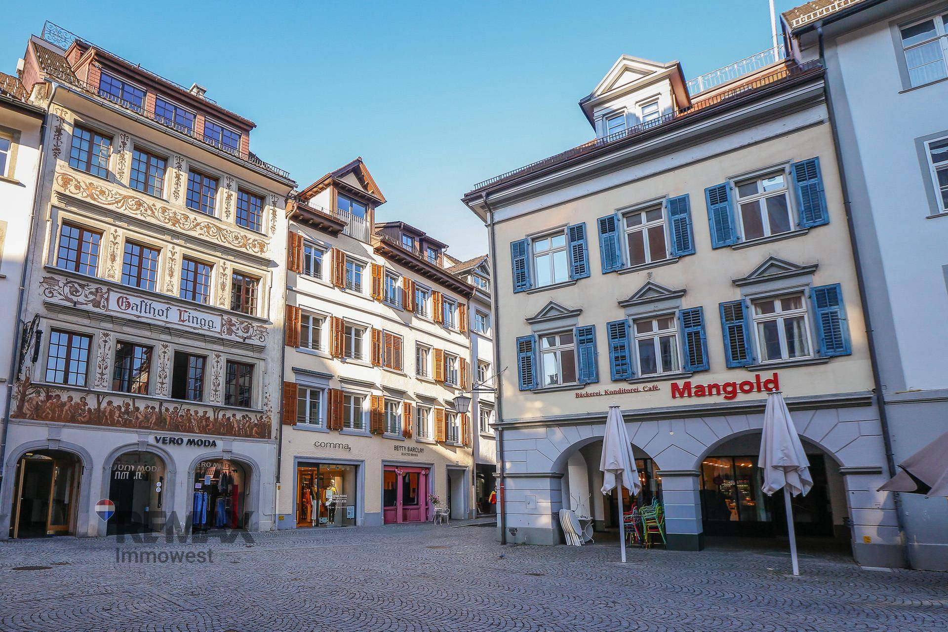 Historische Gebäude in einer belebten Altstadtgasse mit Geschäften und Cafés.