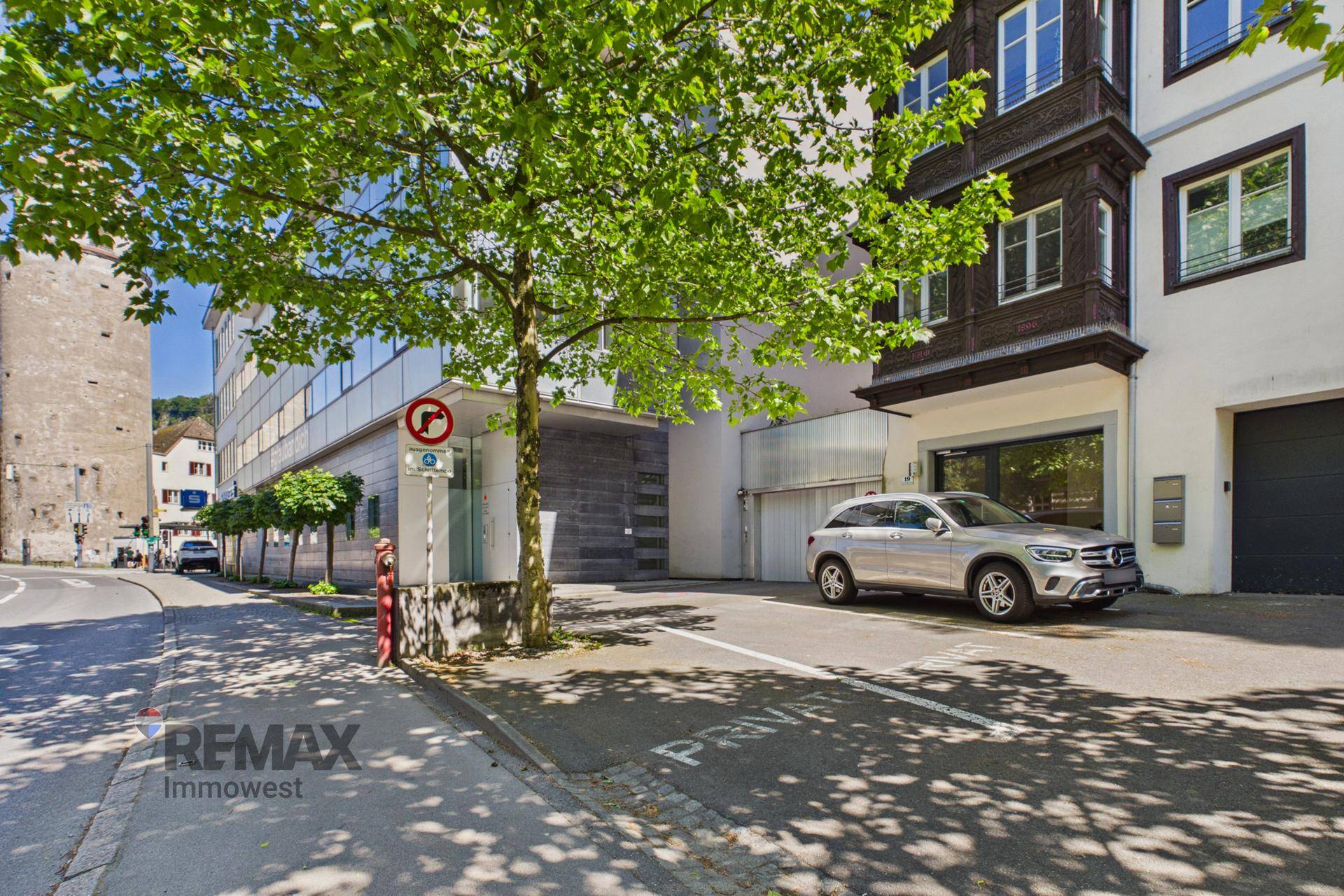 Stadtansicht mit Parkplatz vor einem Gebäude und altem Turm im Hintergrund.