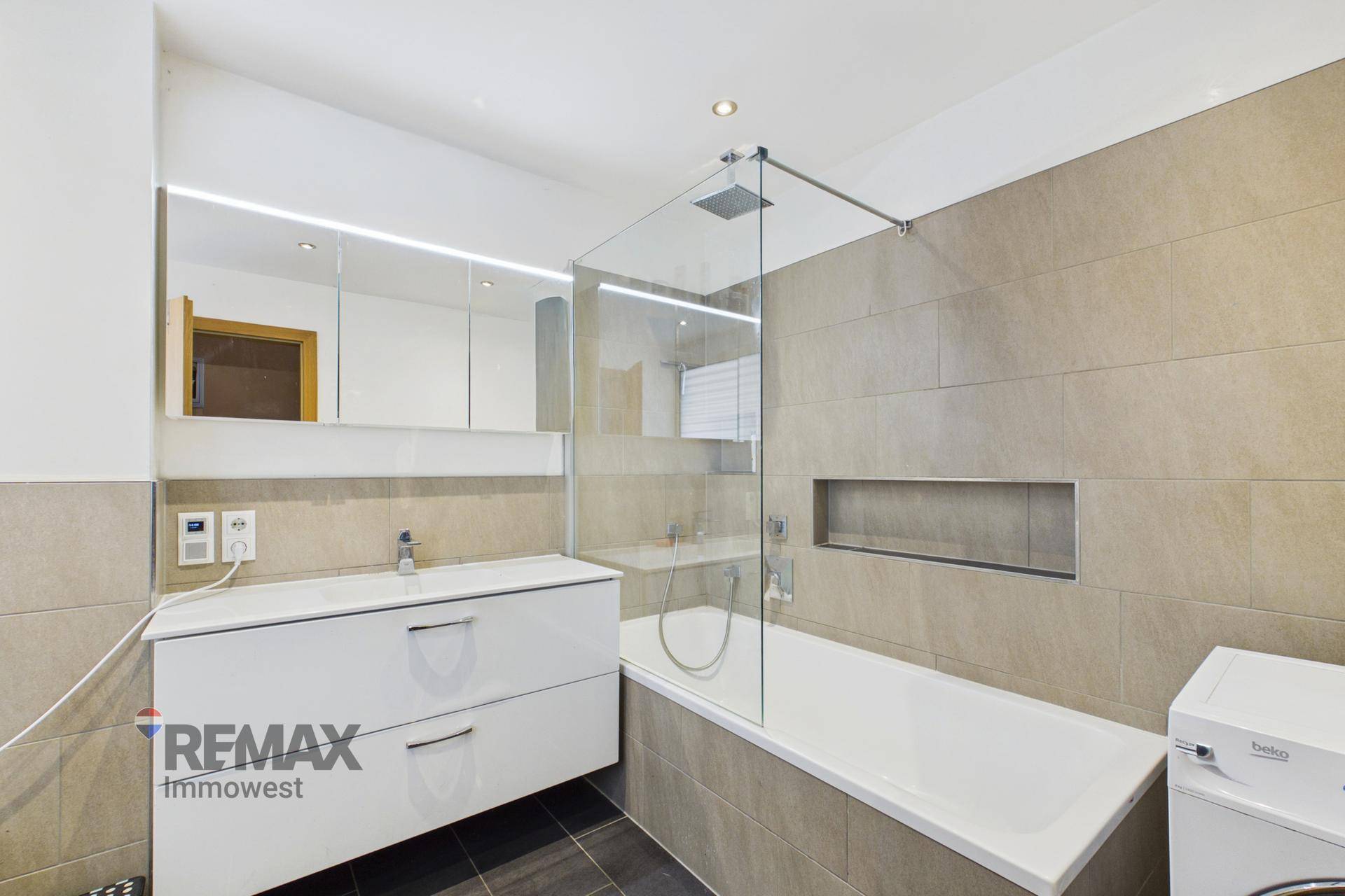 Modernes Badezimmer mit Badewanne, Duschabtrennung, Einzelwaschbecken und Spiegelschrank.
