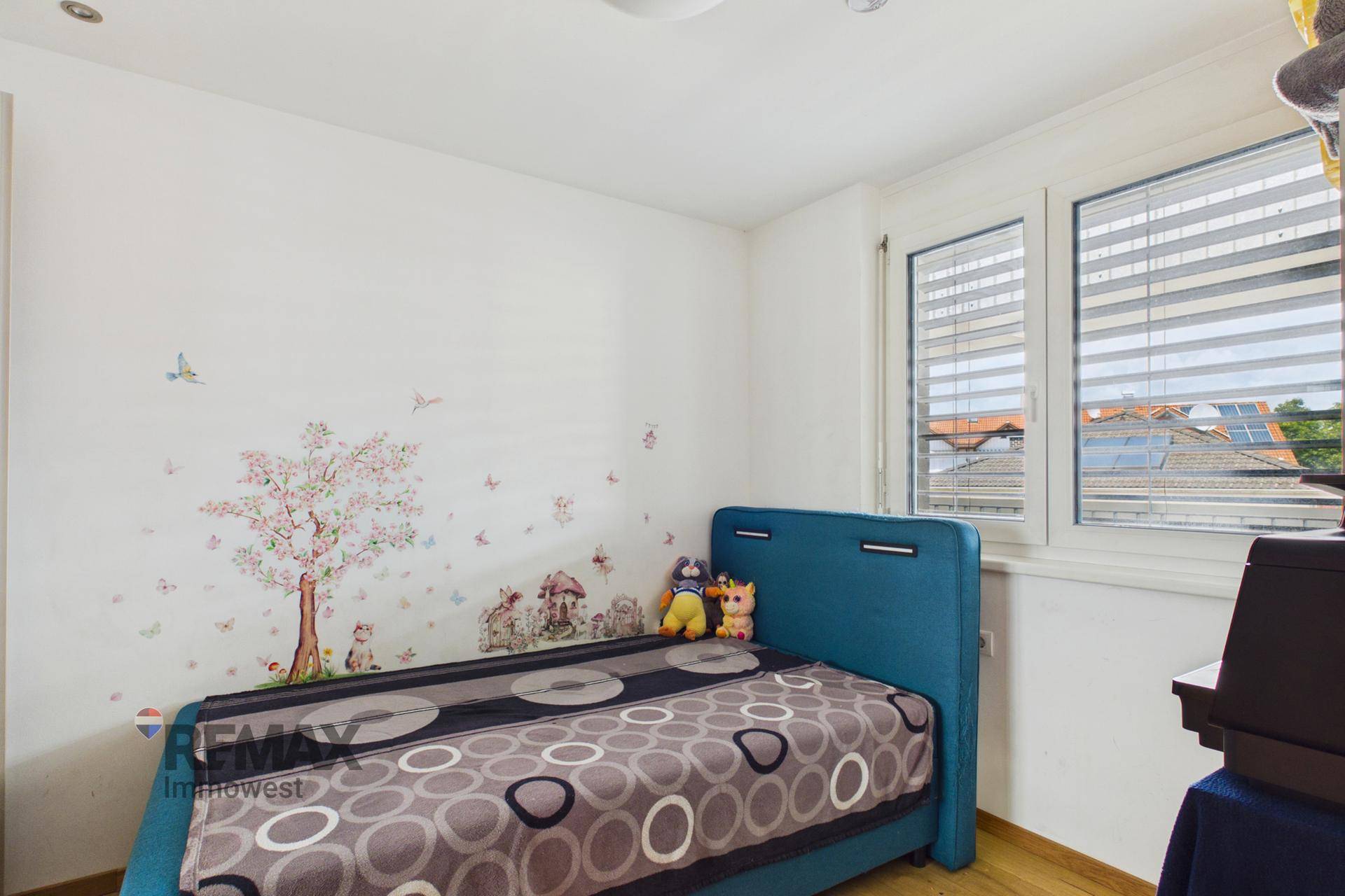 Kinderzimmer mit Einzelbett, Wanddekoration und Fenster mit Blick ins Grüne.