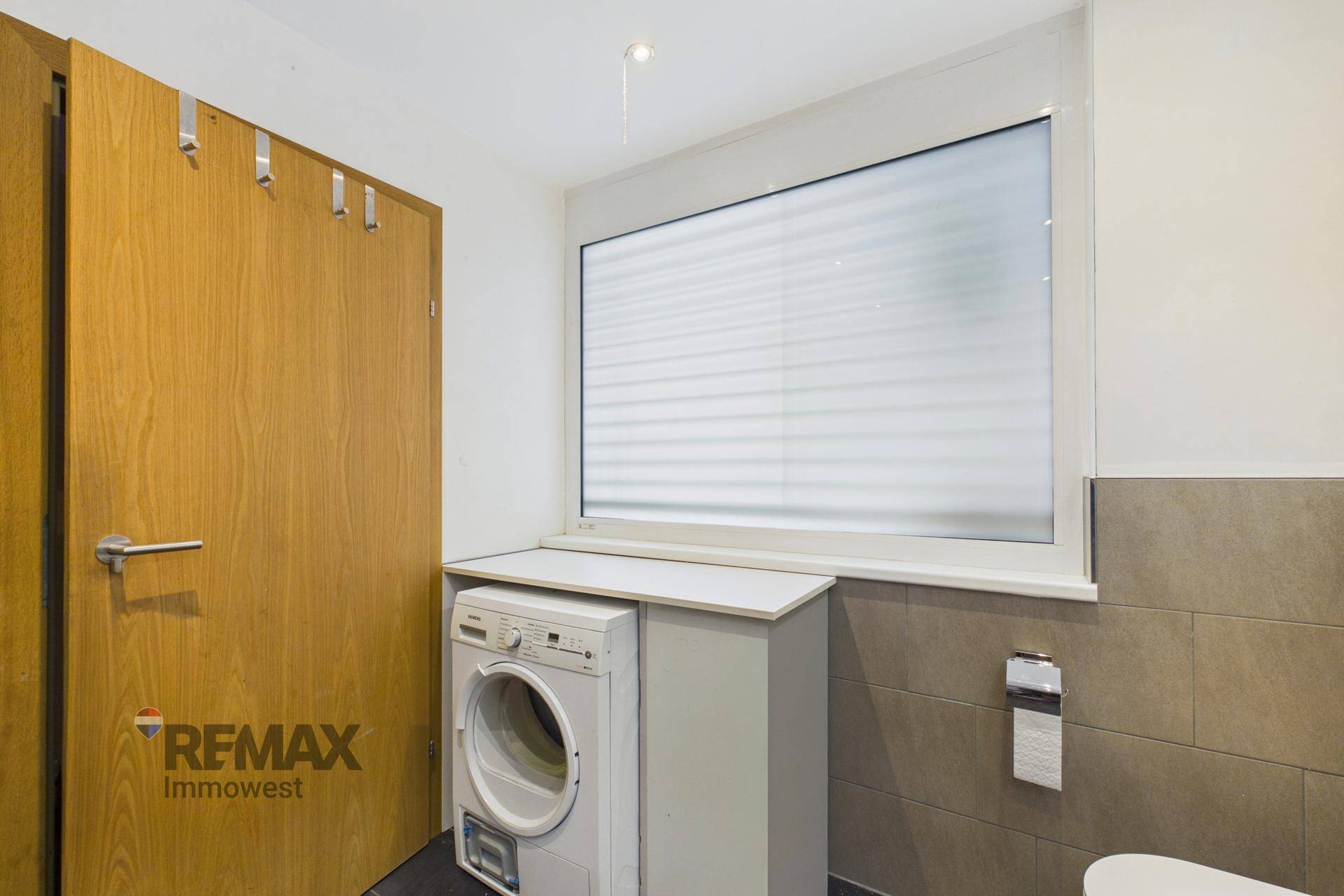 Badezimmer mit Waschmaschine, Toilette und einem Fenster für Tageslicht.