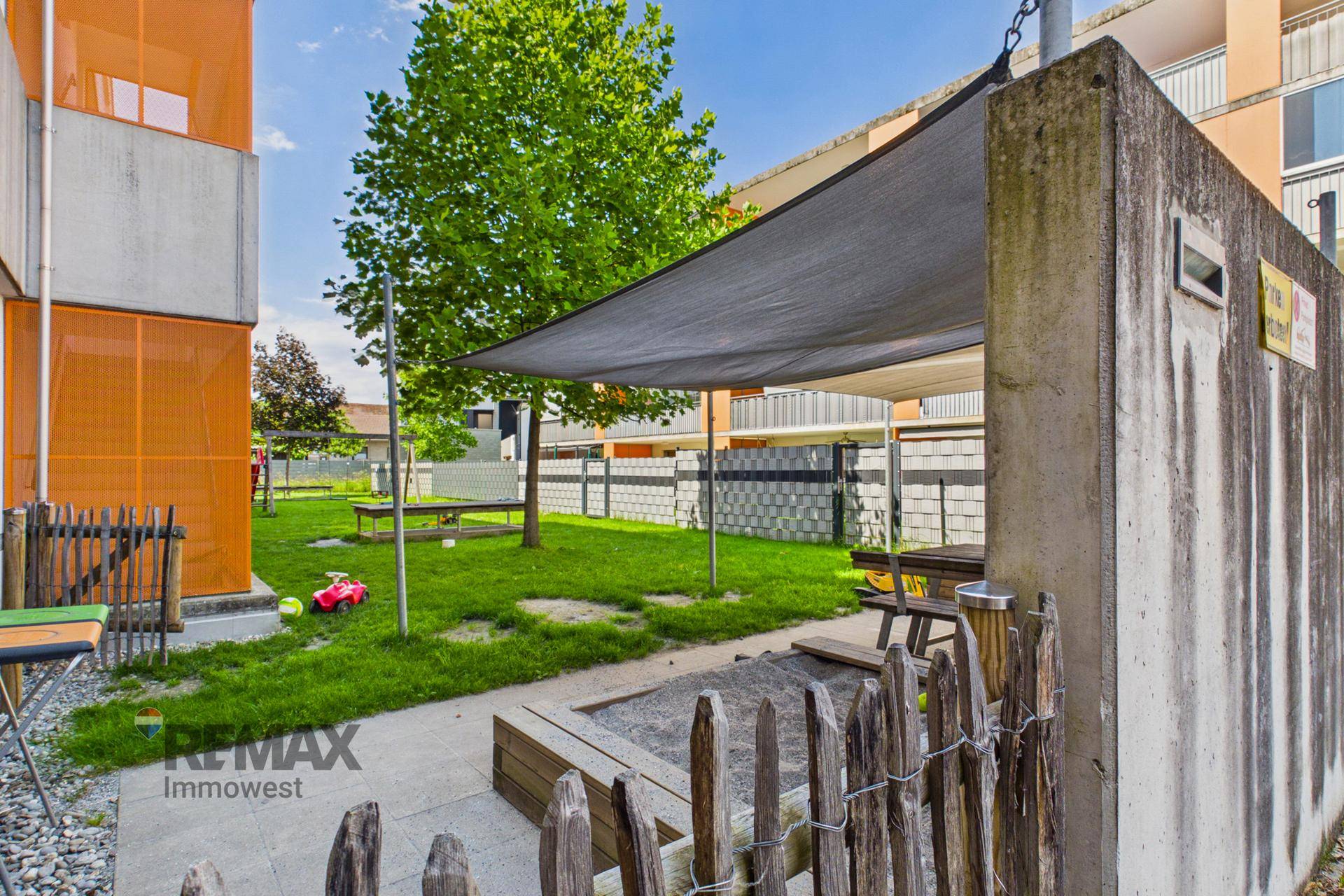 Gemeinschaftlicher Gartenbereich mit Sandkasten, Sitzgelegenheiten und Sonnenschutz.