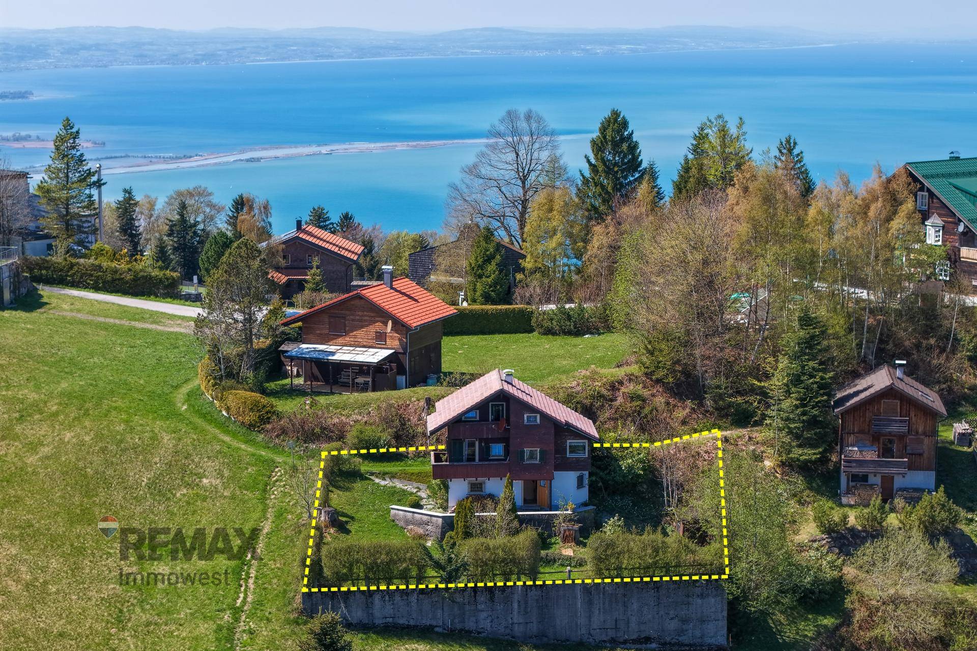Luftaufnahme eines Hauses mit markiertem Grundstück und weitem Blick auf einen See und die Umgebung.