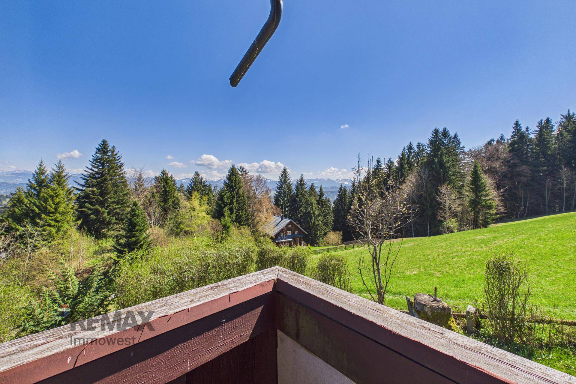Panoramablick vom Balkon über grüne Wälder und ferne Berge unter blauem Himmel.