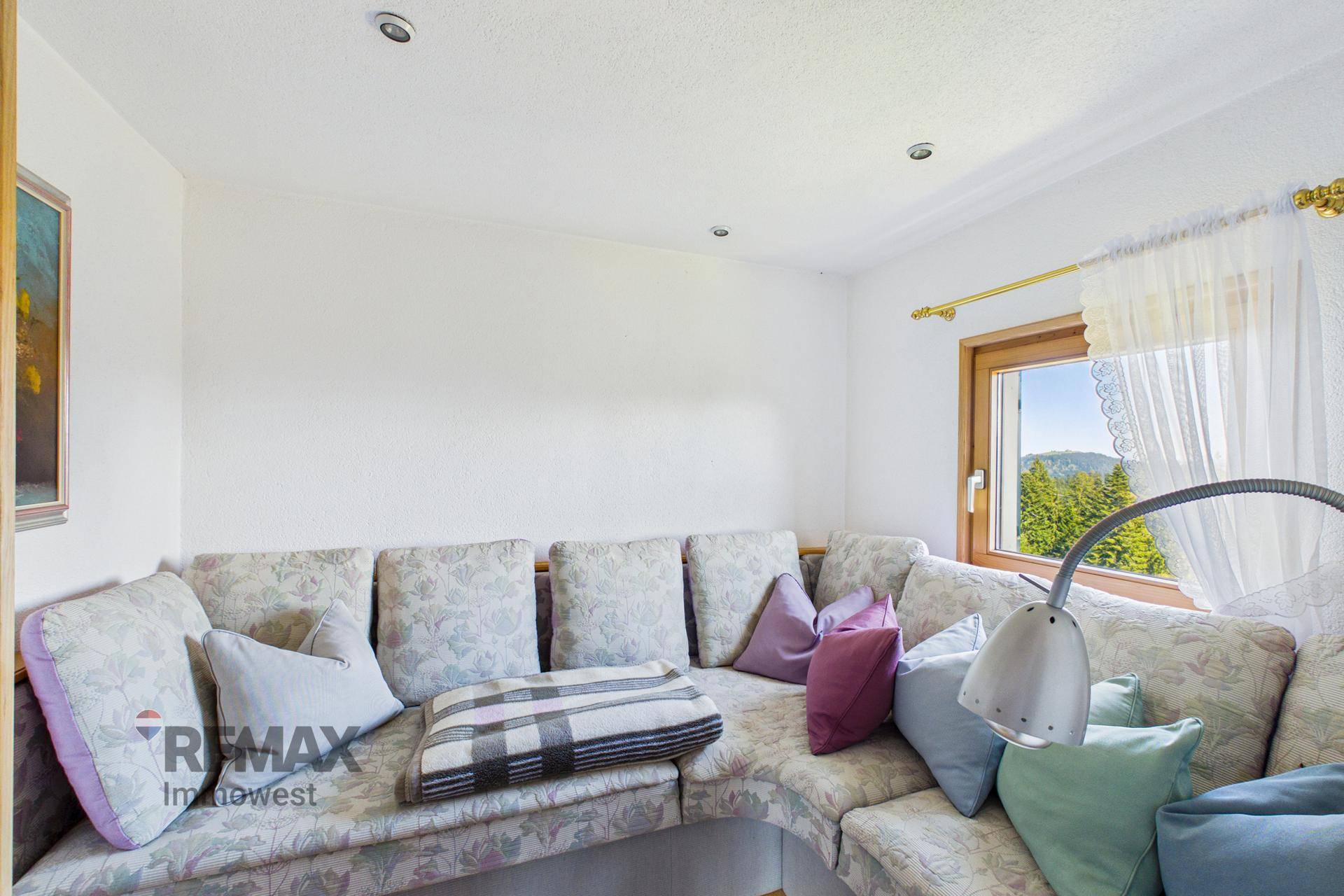 Gemütliche Sitzecke im Wohnzimmer mit vielen Kissen und Fensterblick in die Natur.