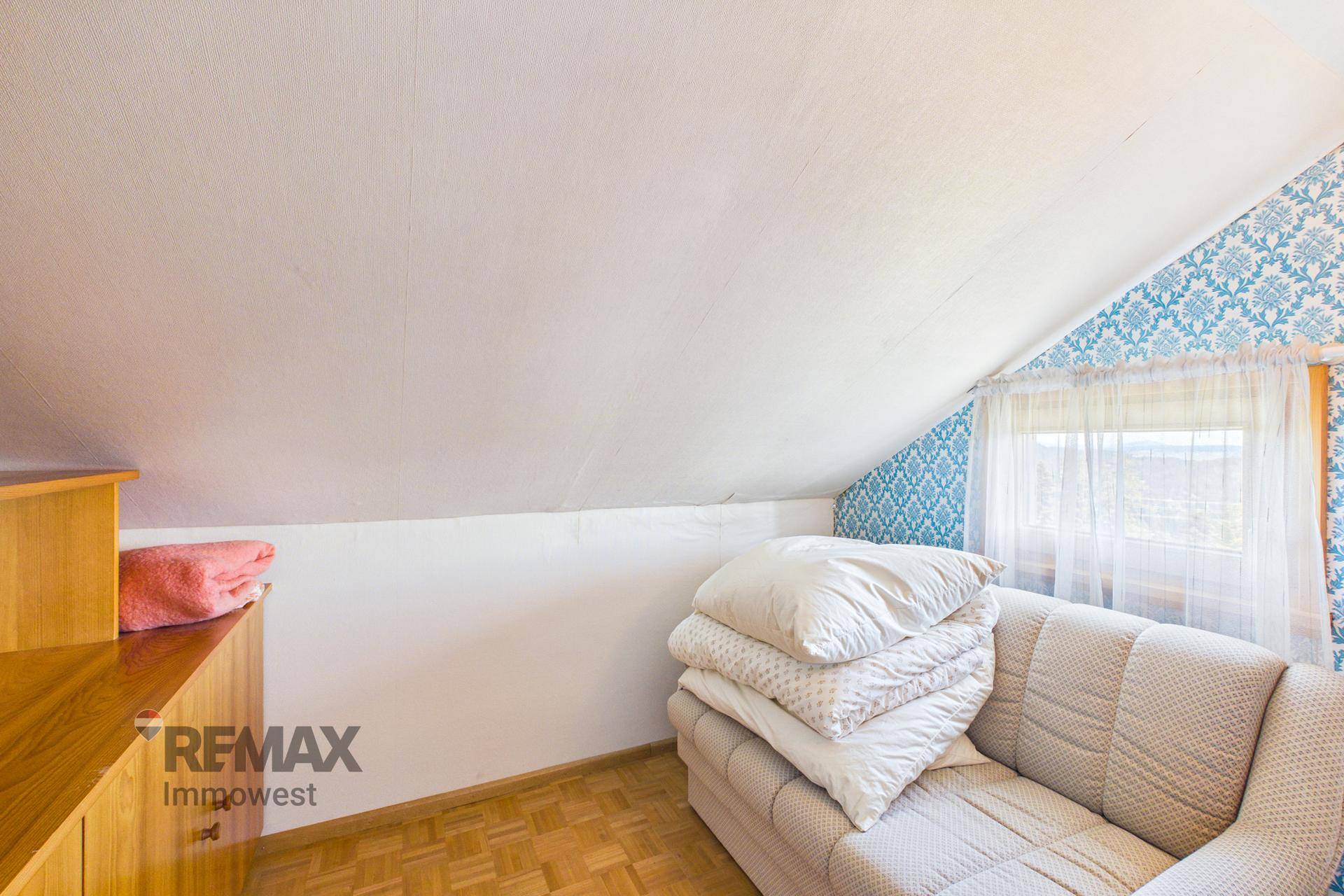 Dachgeschossraum mit schrägen Wänden, Sofa und Stauraum, ideal als Gästezimmer.