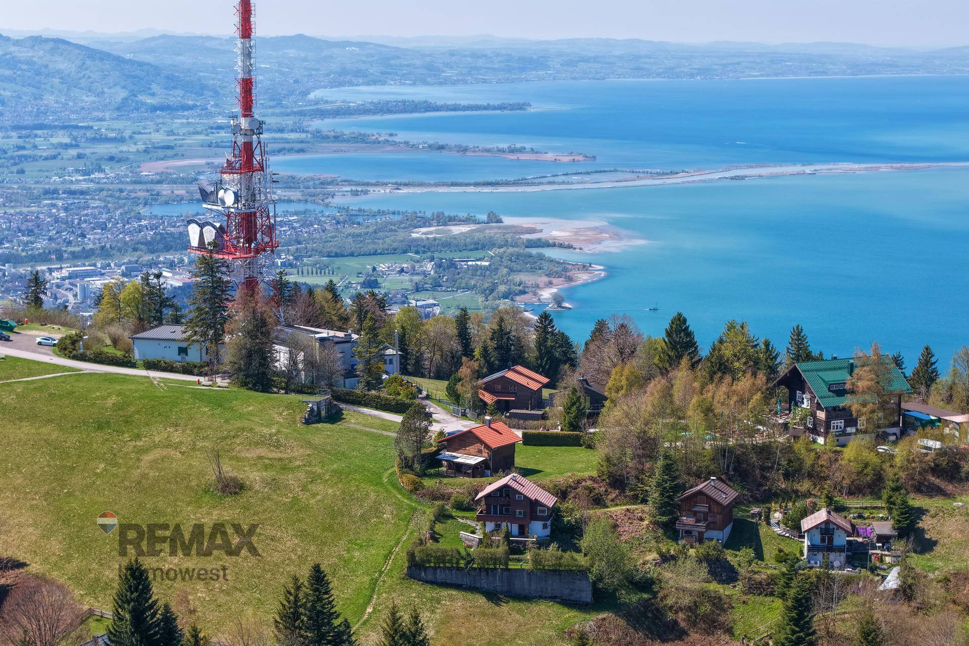Luftaufnahme der Umgebung mit Häusern, einem Sendeturm und einem See im Hintergrund.
