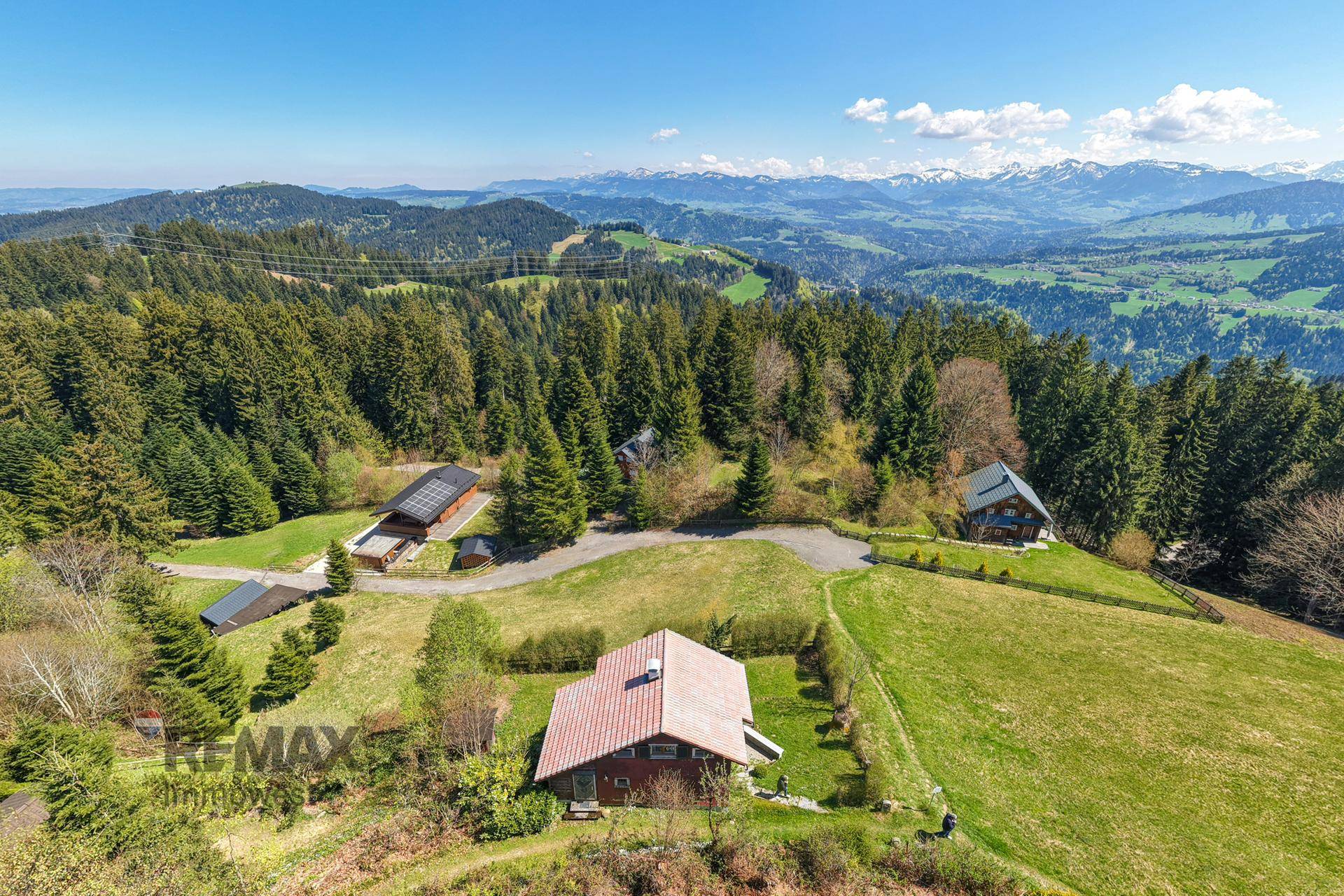 Weitläufige Luftaufnahme der Liegenschaft inmitten grüner Hügel und Wälder mit Bergblick.