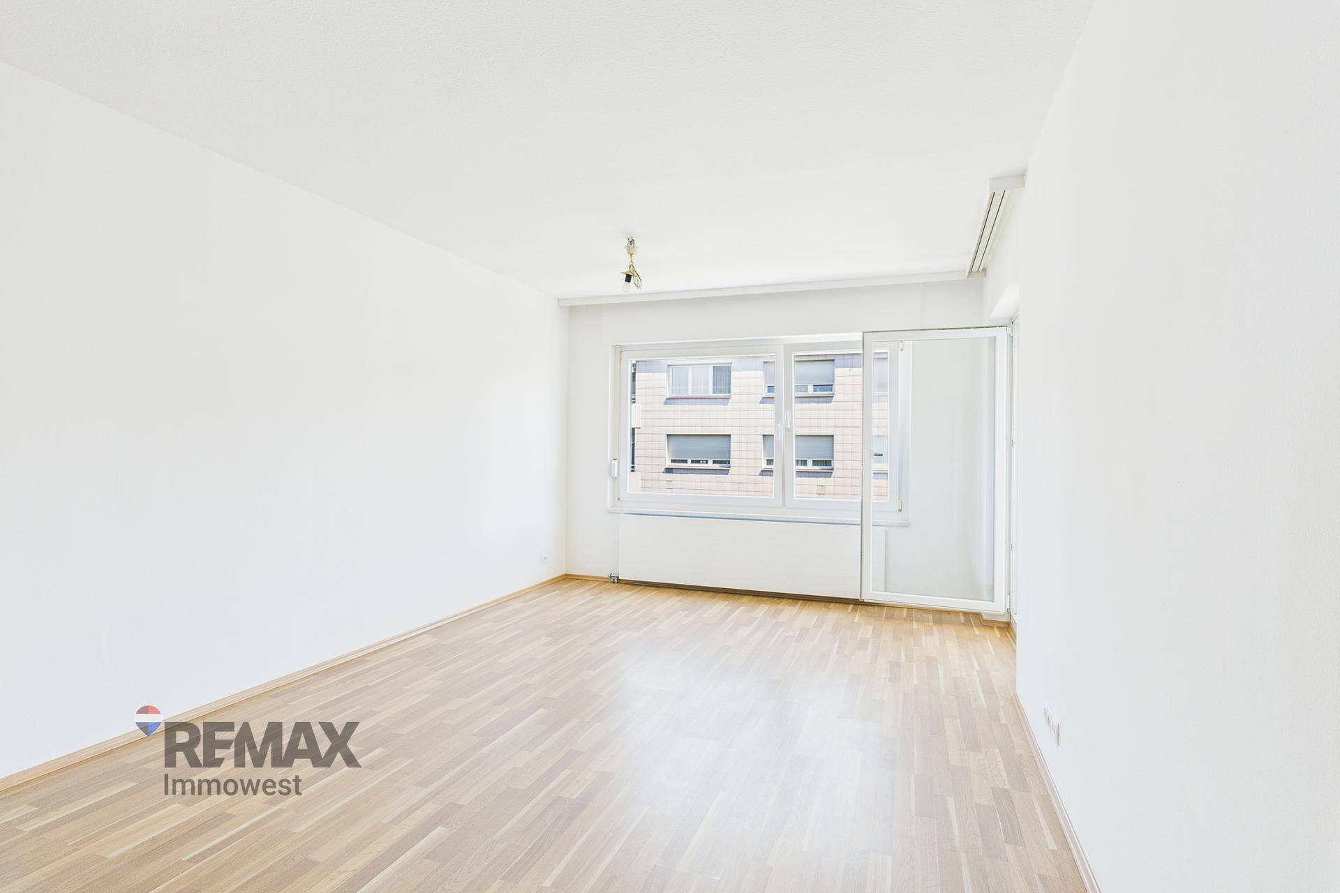 Leerer Raum mit Holzboden, weißen Wänden und einem Fenster mit Schiebetür.