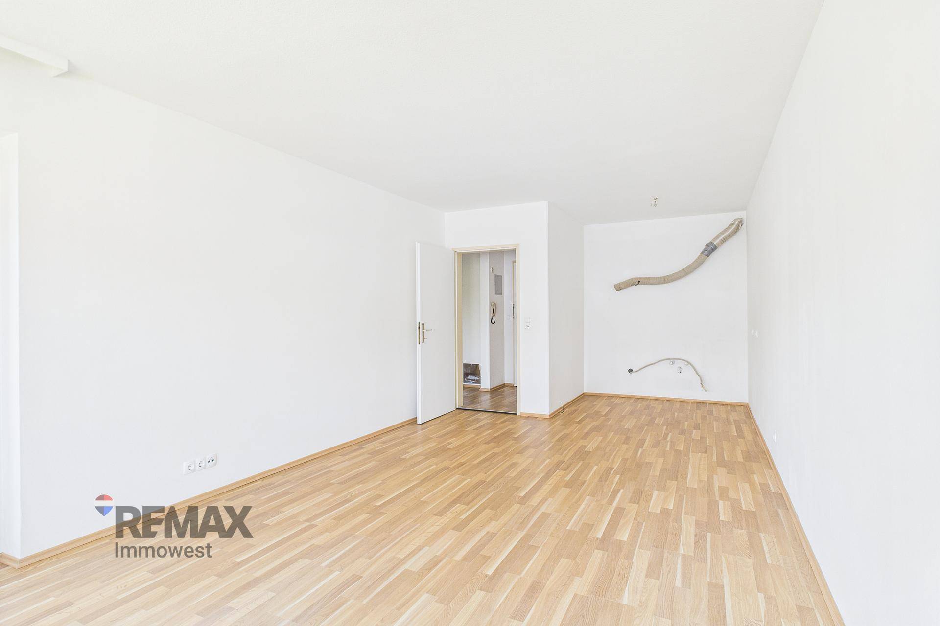 Heller, leerer Raum mit Holzboden und einer offenen Tür, die zu einem weiteren Zimmer führt.