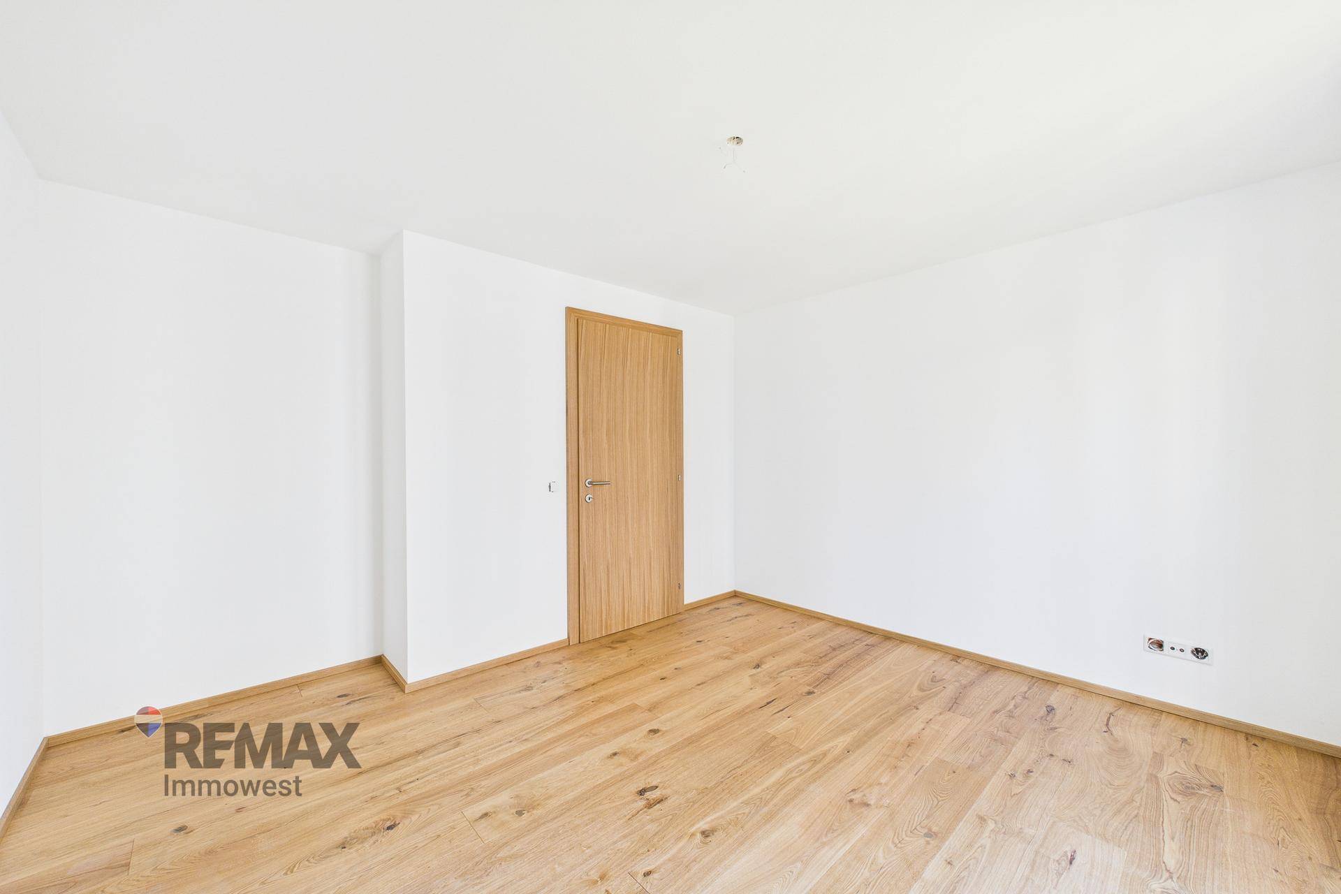 Leeres Zimmer mit hellem Parkettboden und einer modernen Holztür, bereit zur individuellen Gestaltung.