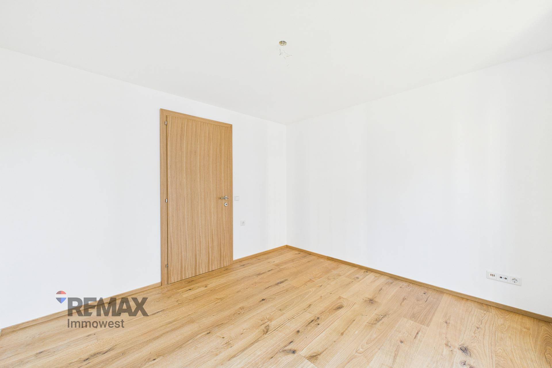 Geräumiges Zimmer mit hellem Parkettboden und einer schlichten Holztür, ideal für vielfältige Nutzung.