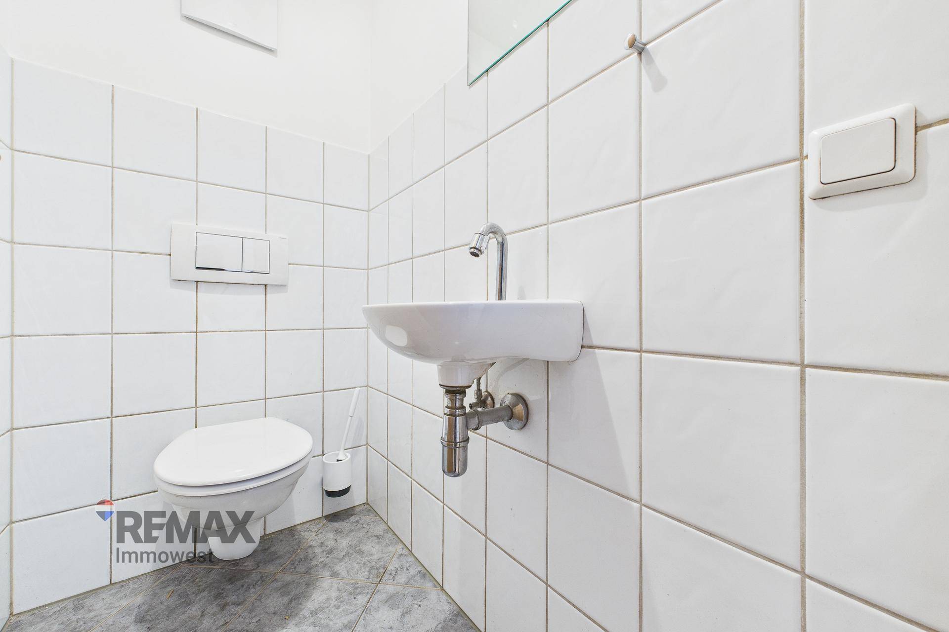 Sauber gefliestes Gäste-WC mit wandhängender Toilette und kleinem Handwaschbecken.