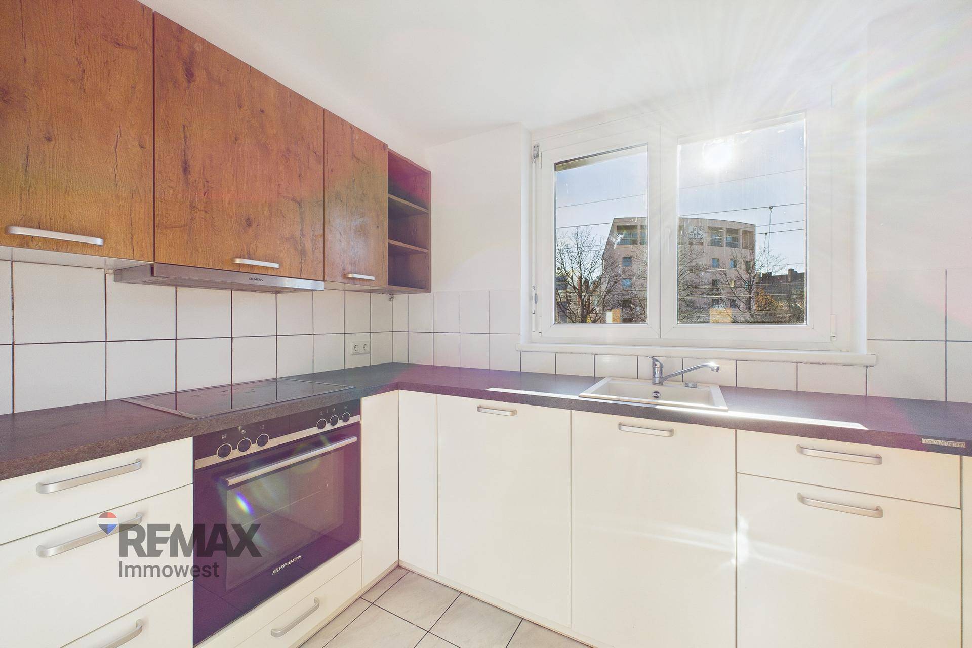 Helle Küche mit weißen Schränken, Holzdetails und integriertem Backofen, durchflutet von Sonnenlicht.